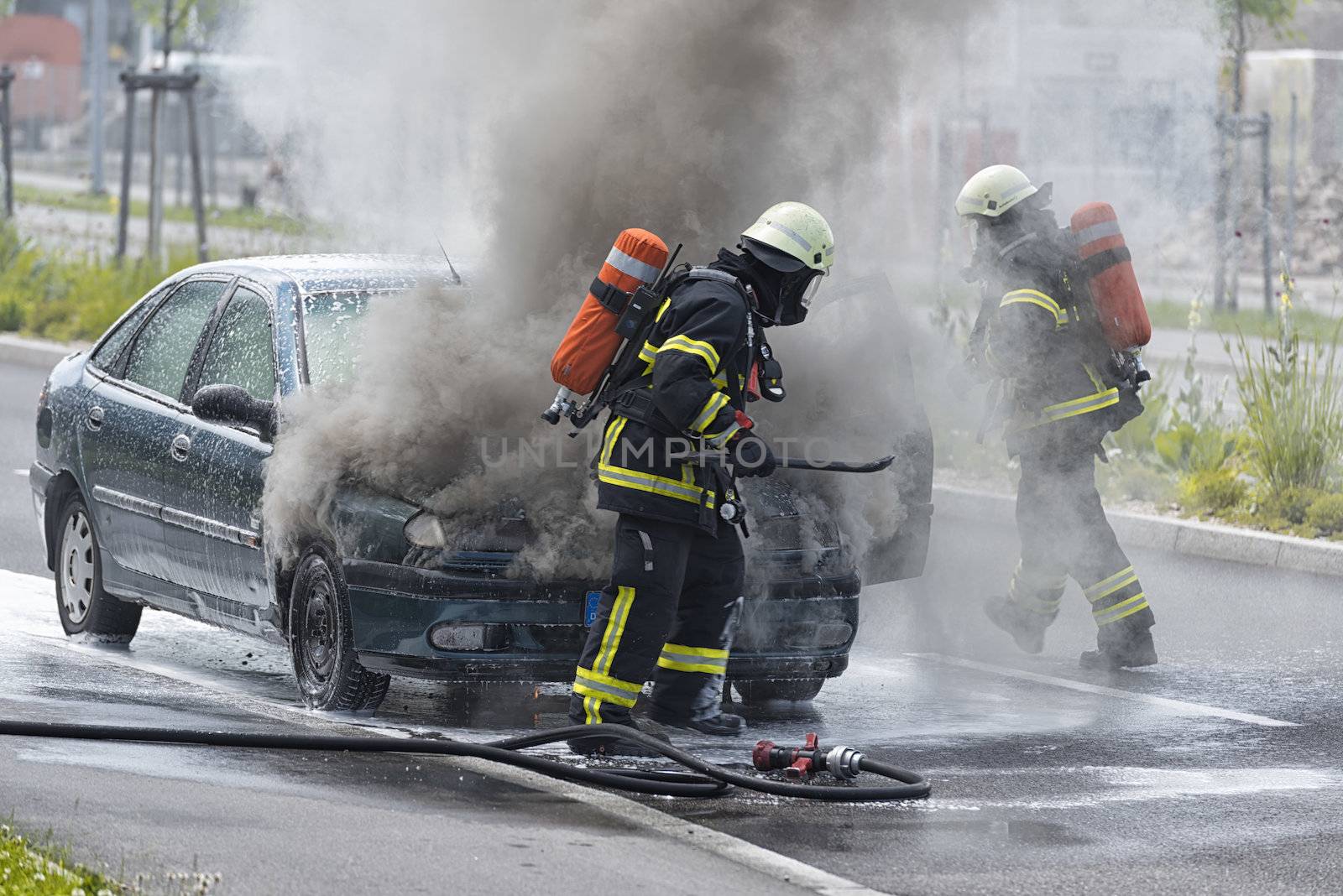 Burning motor vehicle been put out by firemen in protective clothing
