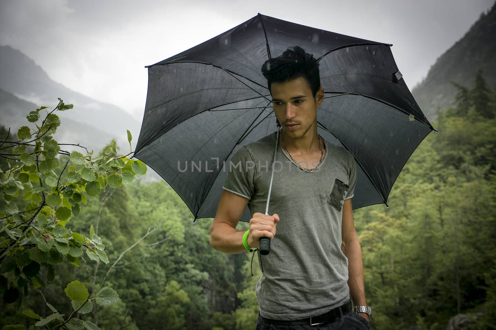 Smiling handsome young man holding an umbrella on a stormy day as he takes a walk along a trail in the mountains