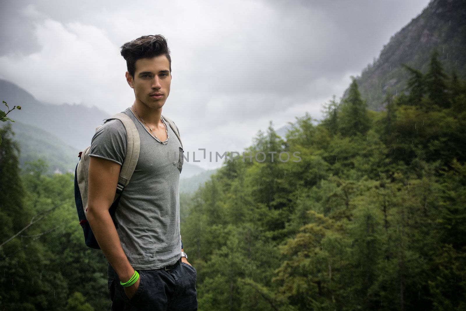 Handsome muscular young man backpacking or hiking in lush green mountain scenery looking at camera