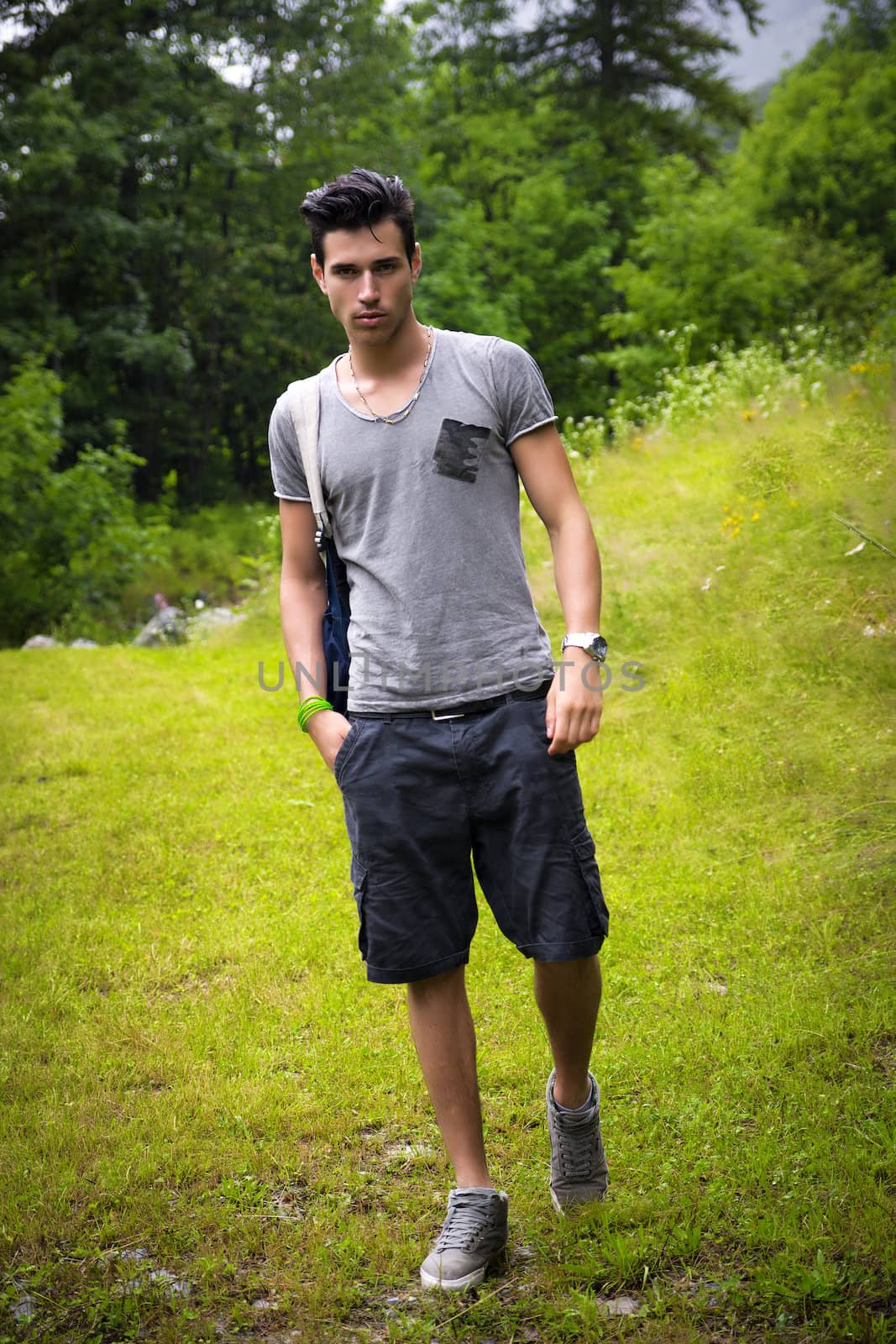 Handsome muscular young man backpacking or hiking in lush green mountain scenery looking at camera