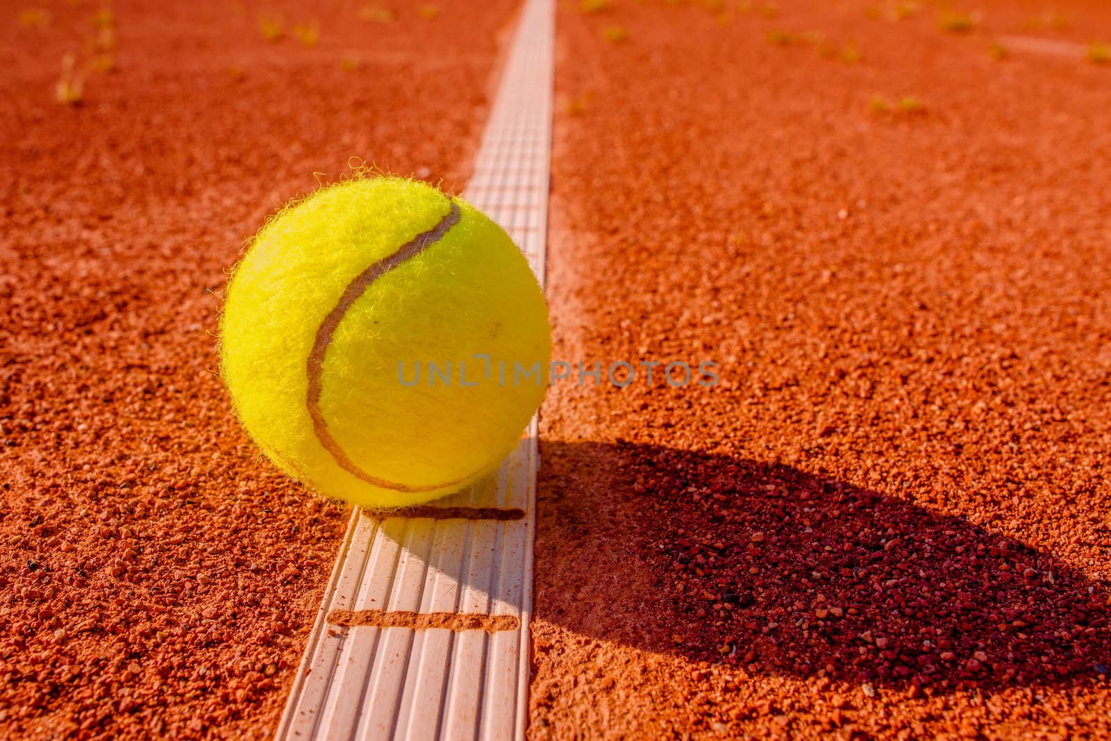 Yellow tennis ball touching the line on red clay court