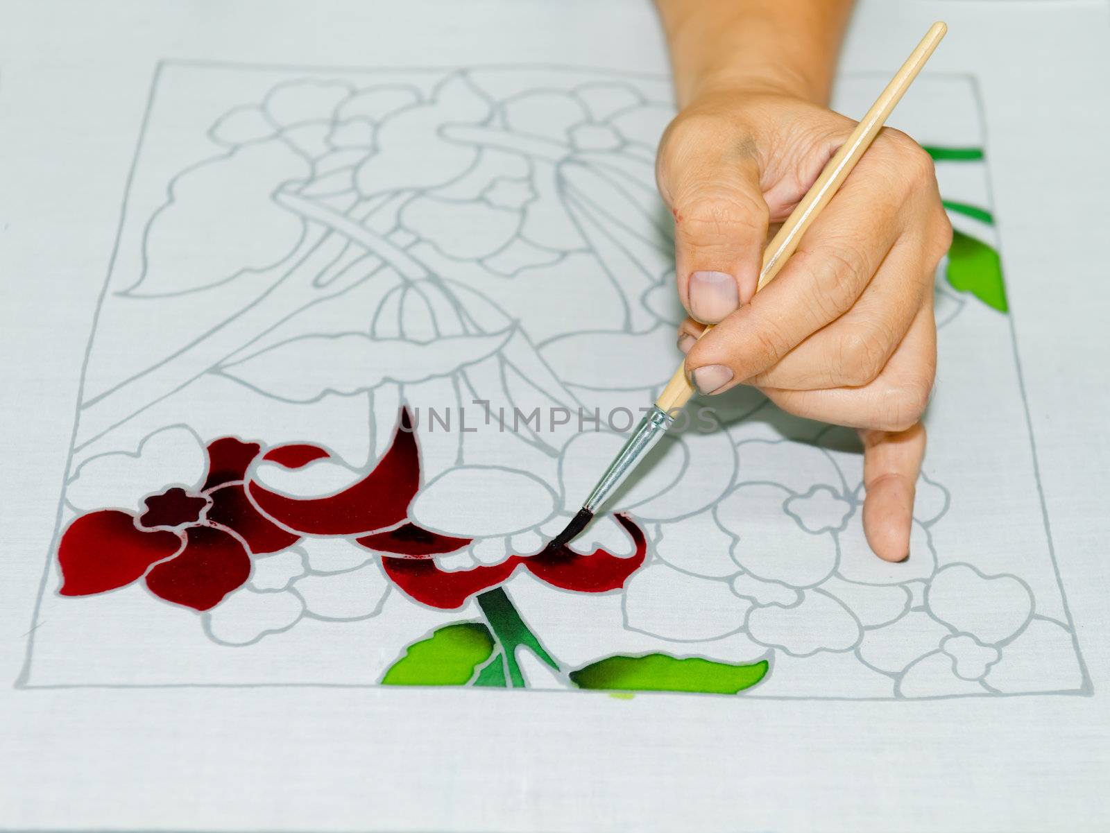 Artist carefully paint the floral flower image on a white batik fabric 