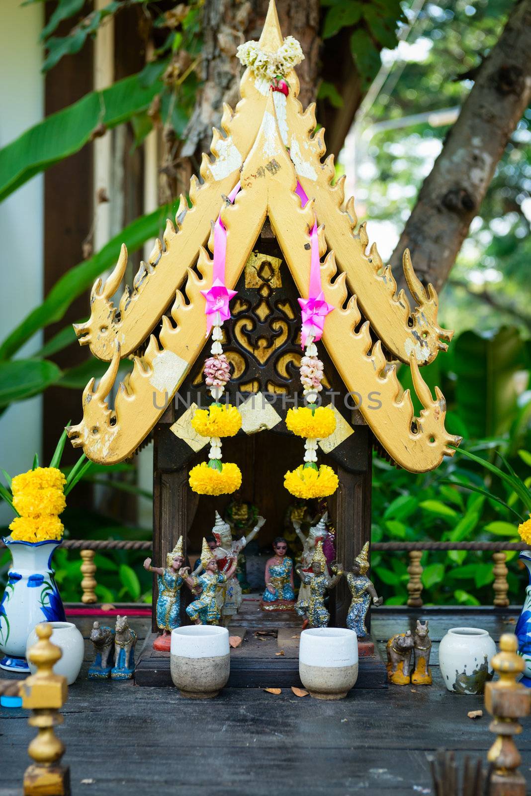 Small spirit house in Thailand with flowers and statuettes