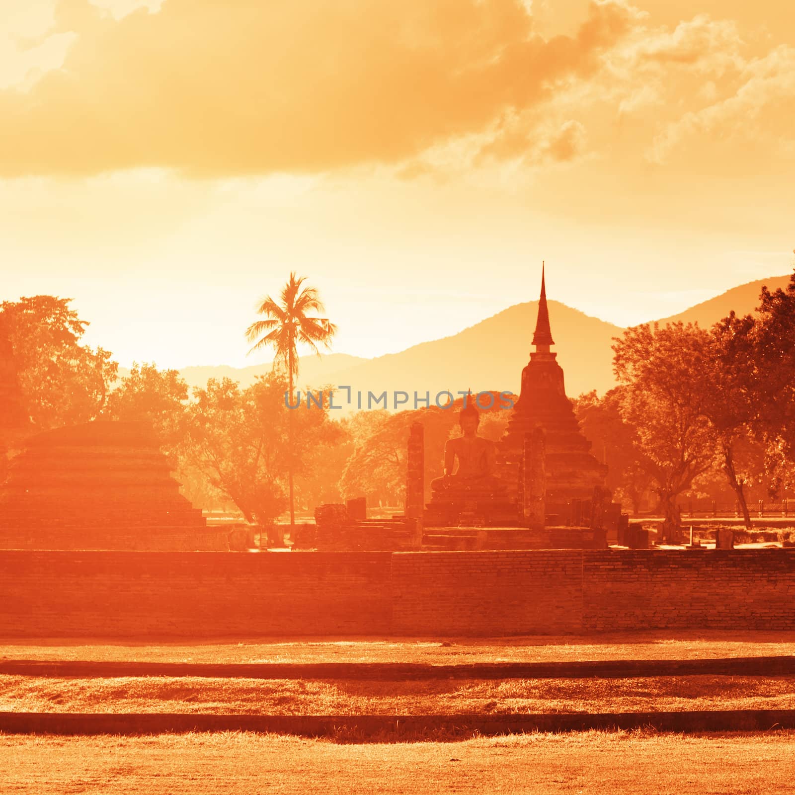 Ruins silhouette of big Buddhist temples with Buddha statues in tropical forest on sunset. Sukhothai historical park, Thailand.