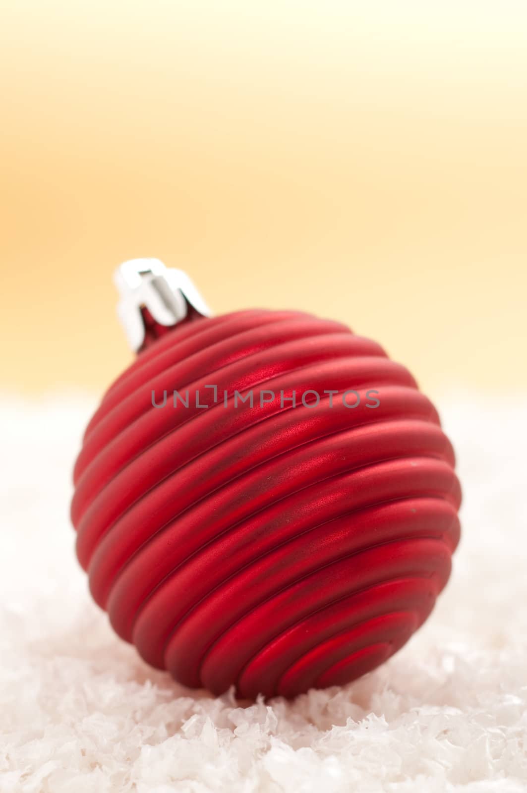 Red christmas ornament in the snow with gold background