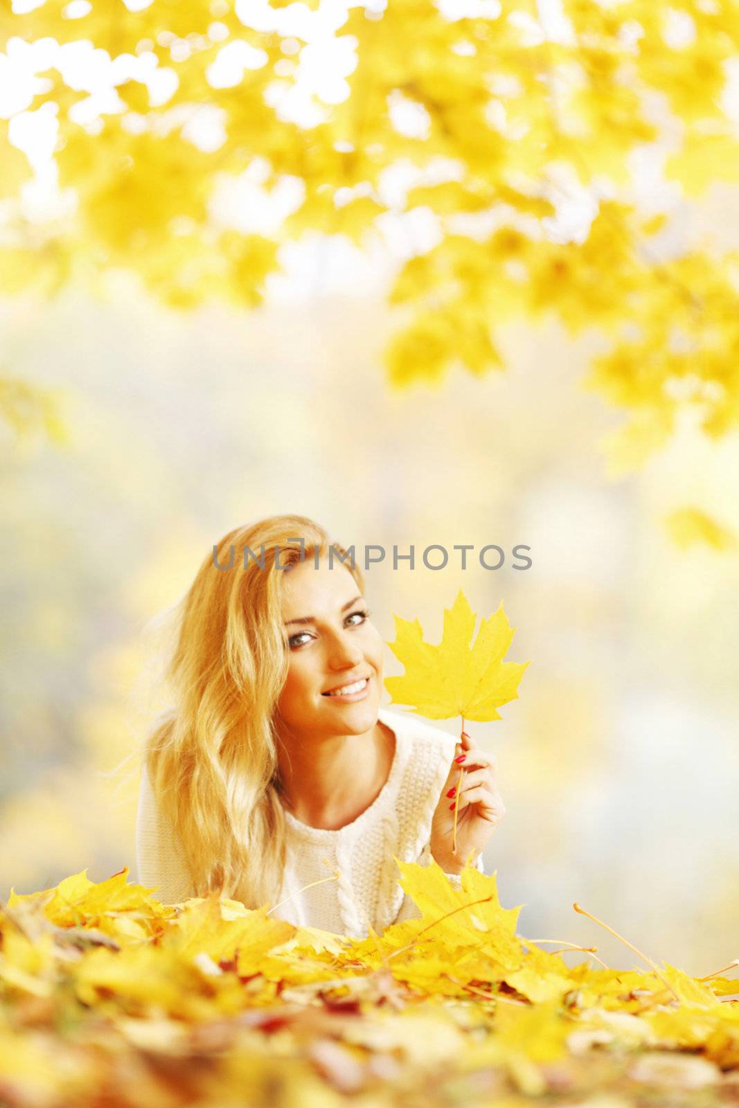 Young woman laying down on the ground covered dry autumnal foliage in beautiful park