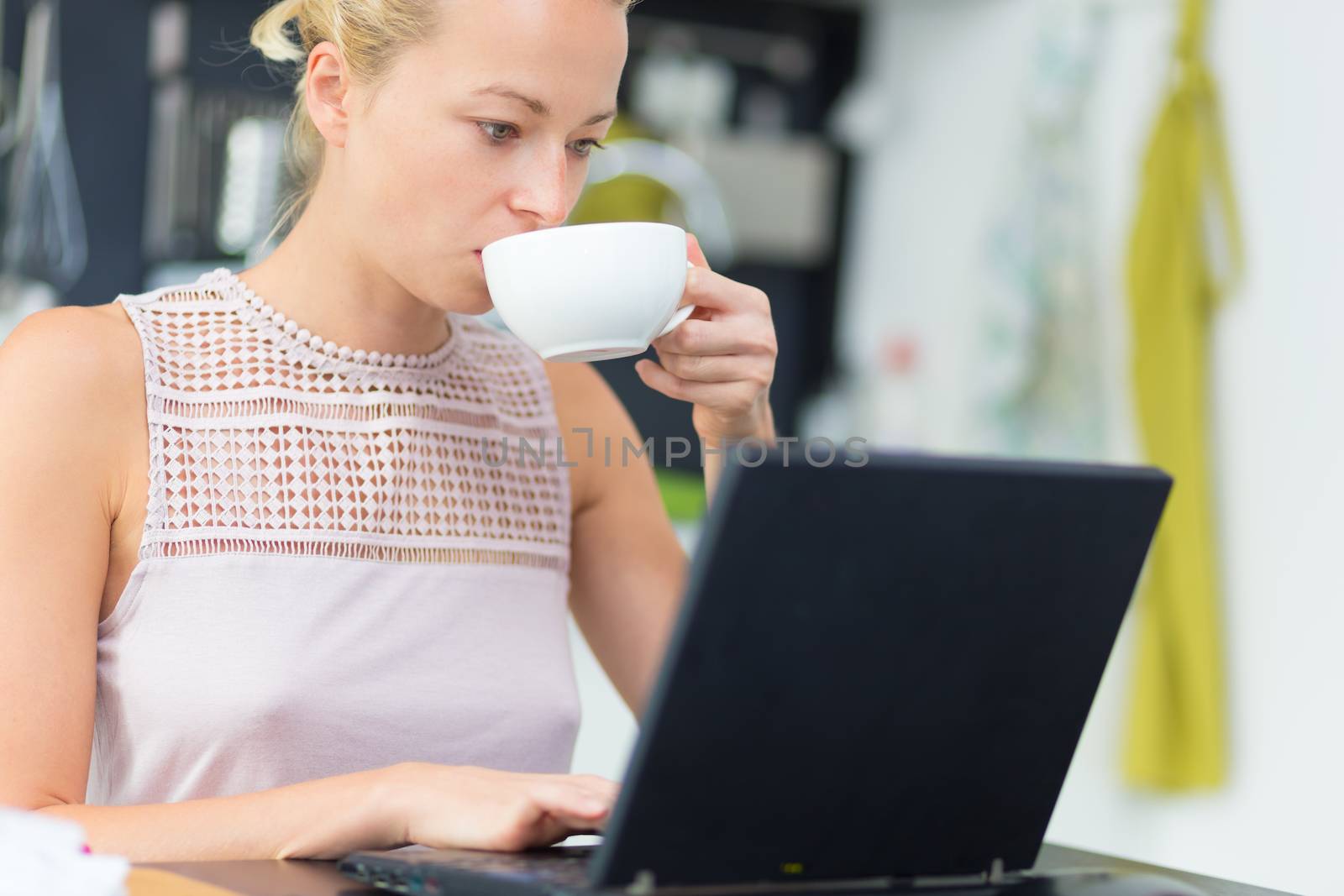 Business woman working remotly from her dining table while having her morning coffee. Home kitchen in the background.