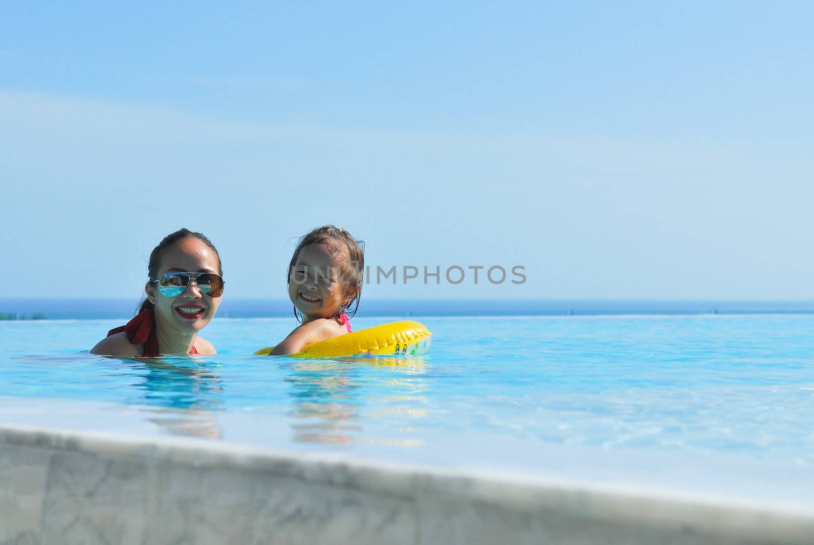 Summer vacations concept. Happy mother and daughter playing in blue water of swimming pool.