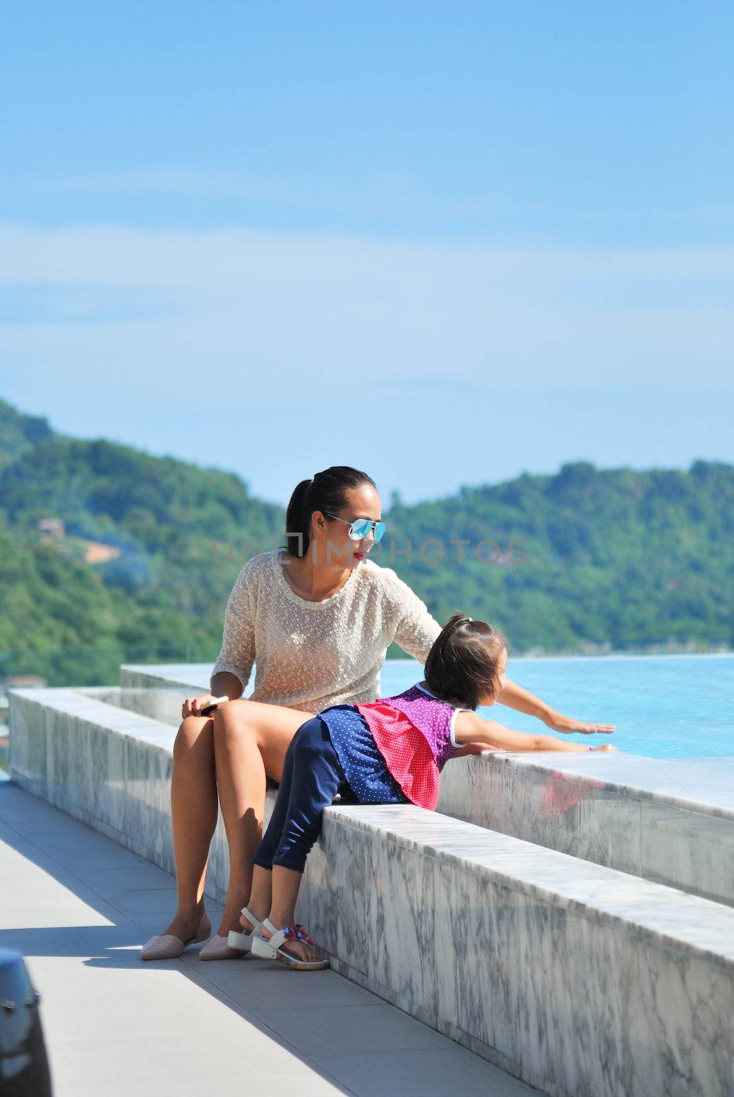 Summer vacations concept. Happy mother and daughter playing in blue water of swimming pool.