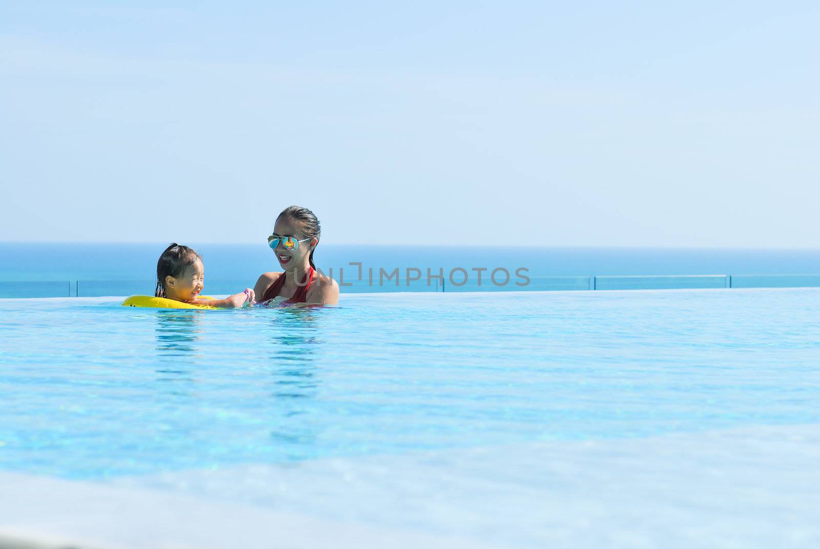 Summer vacations concept. Happy mother and daughter playing in blue water of swimming pool.