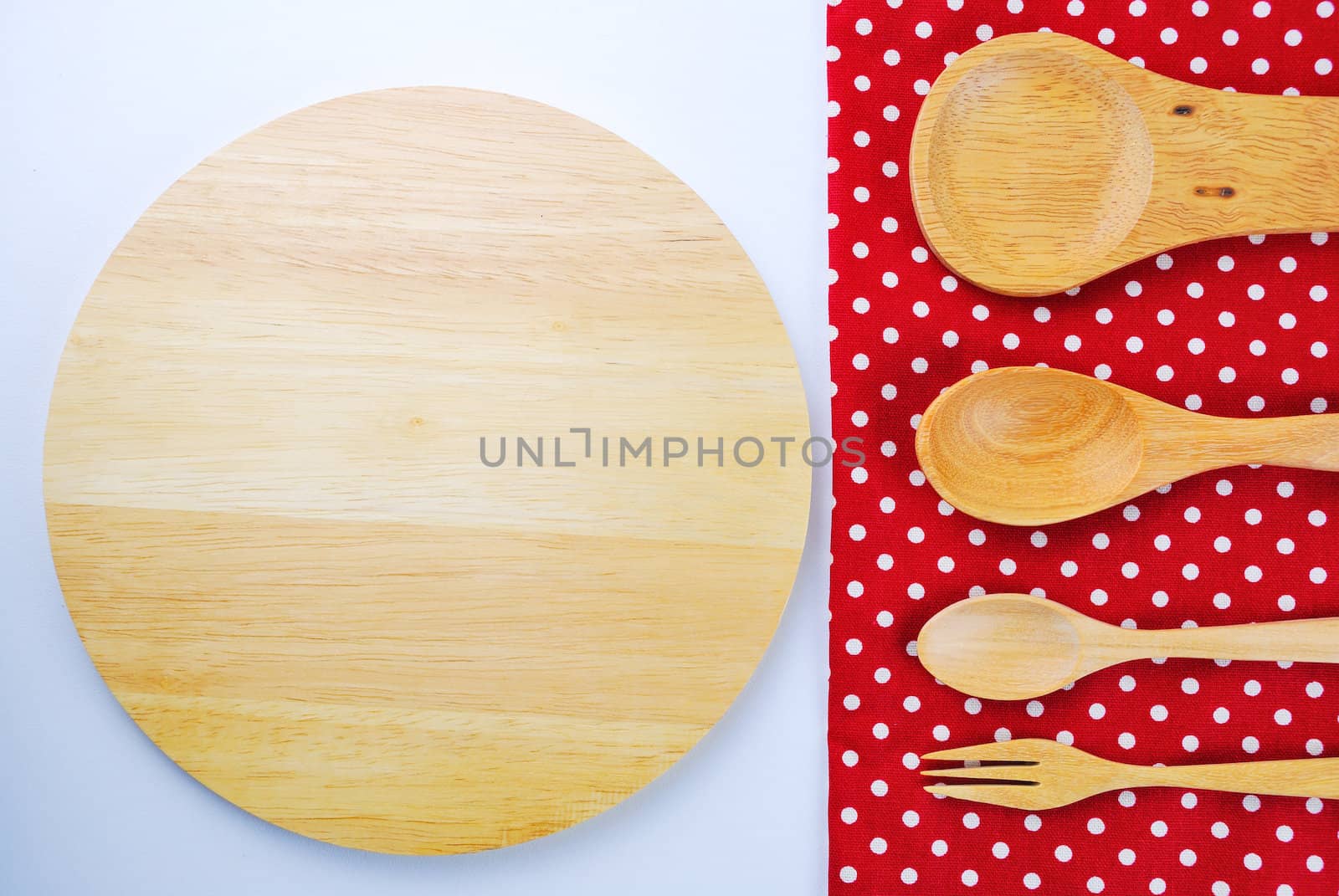 Wooden plate, tablecloth, spoon, fork on table background