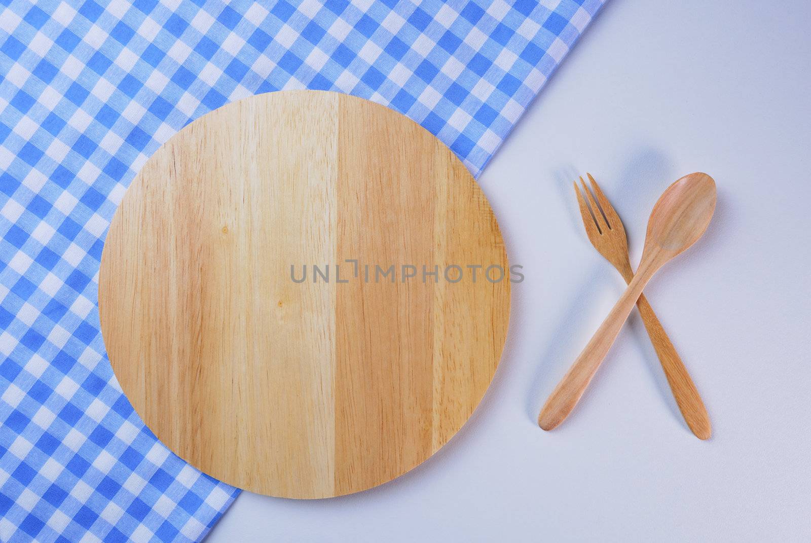 Wooden plate, tablecloth, spoon, fork on table background