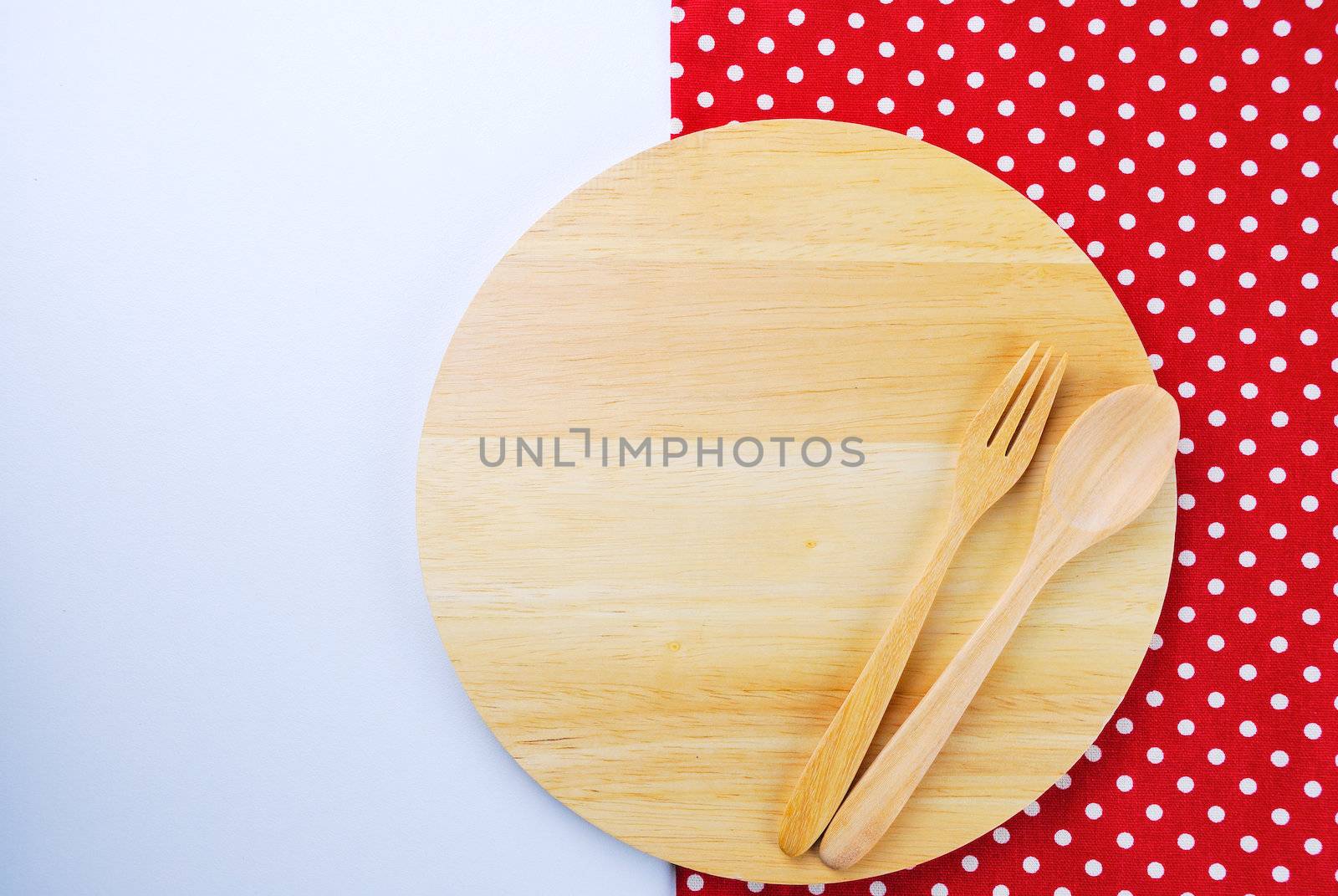 Wooden plate, tablecloth, spoon, fork on table background