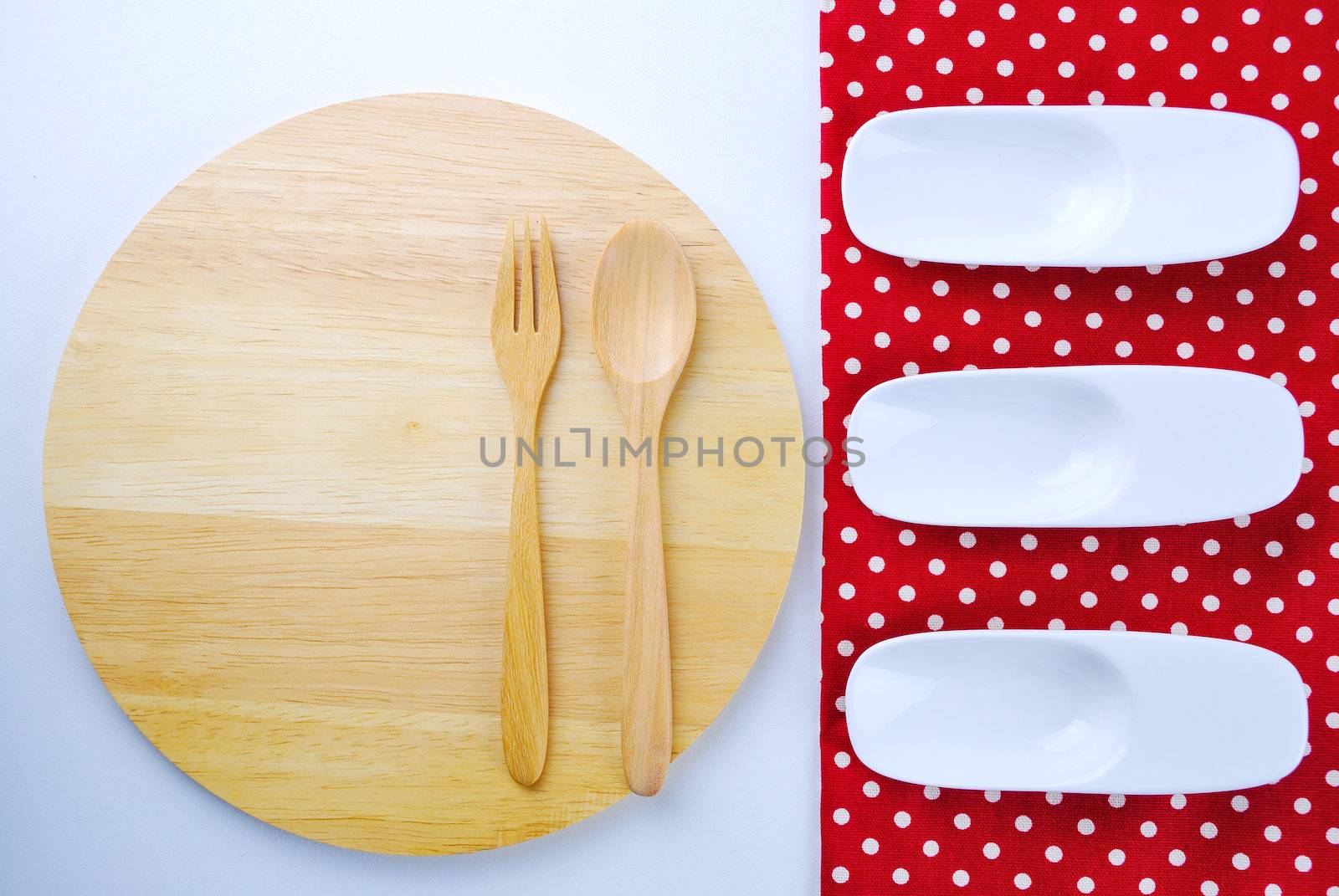 Wooden plate, tablecloth, spoon, fork on table background