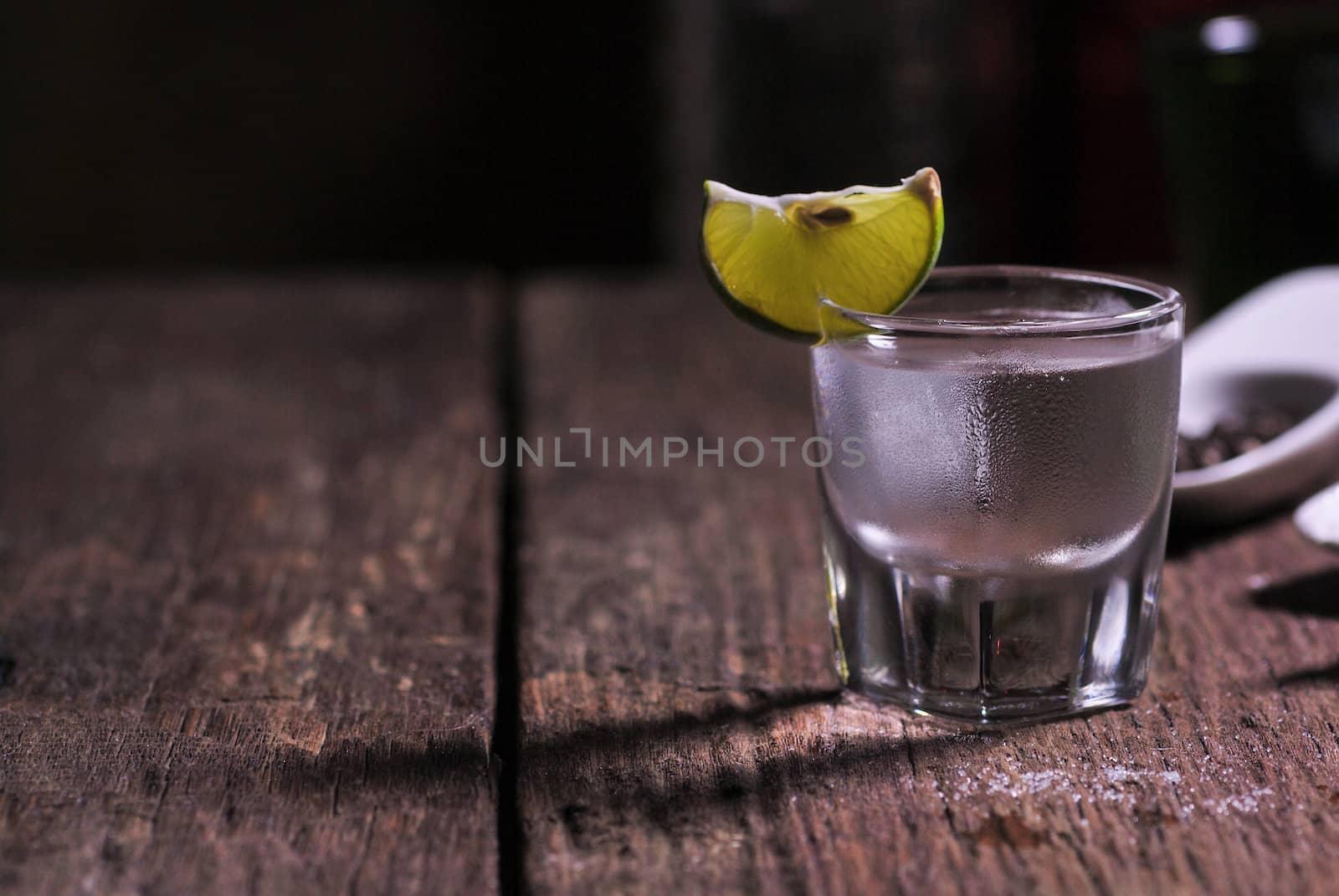 Glass of vodka shot with fresh lime on wooden table