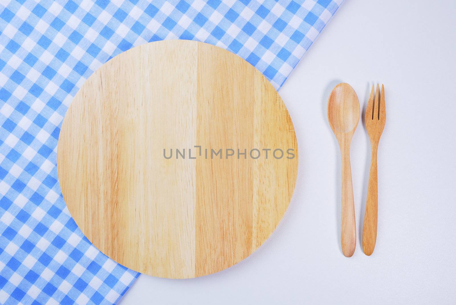 Wooden plate, tablecloth, spoon, fork on table background