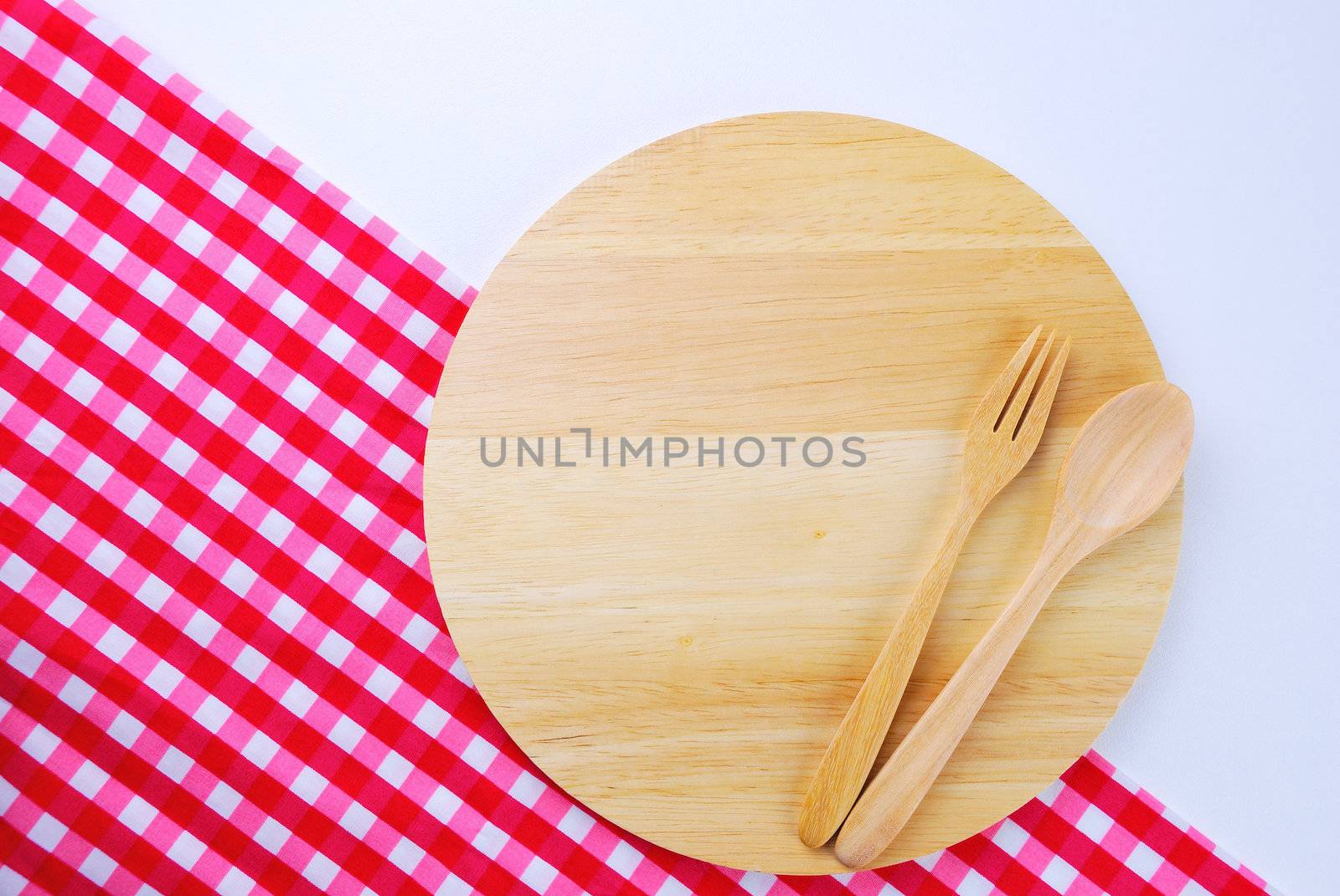 Wooden plate, tablecloth, spoon, fork on table background