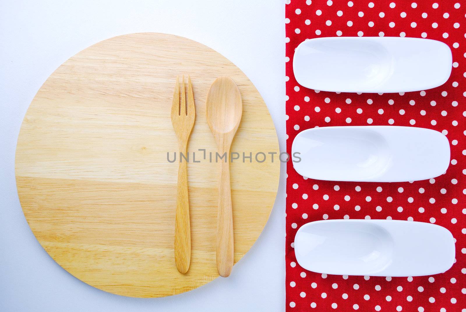 Wooden plate, tablecloth, spoon, fork on table background