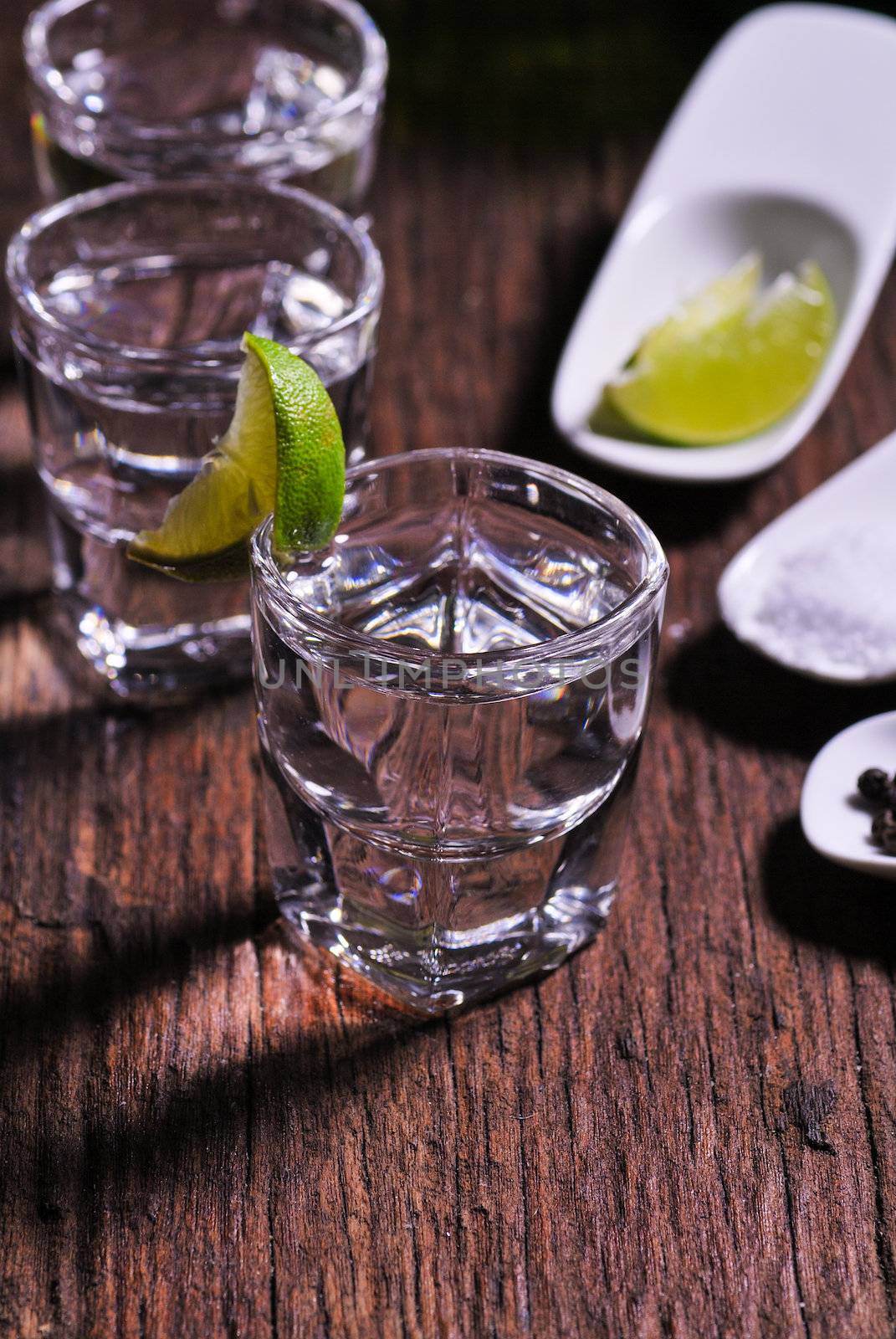 Glass of vodka shot with fresh lime on wooden table