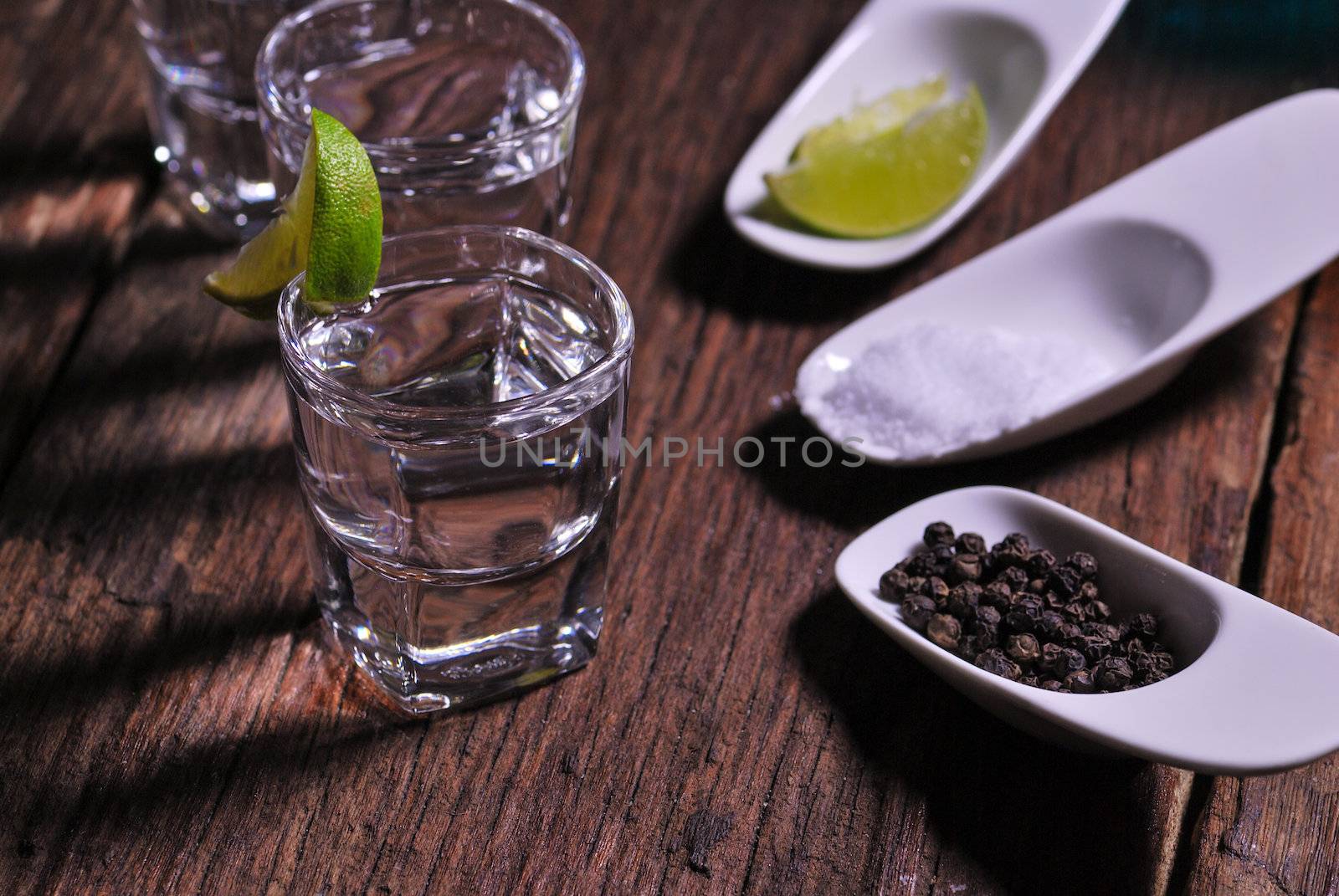 Glass of vodka shot with fresh lime on wooden table by teen00000