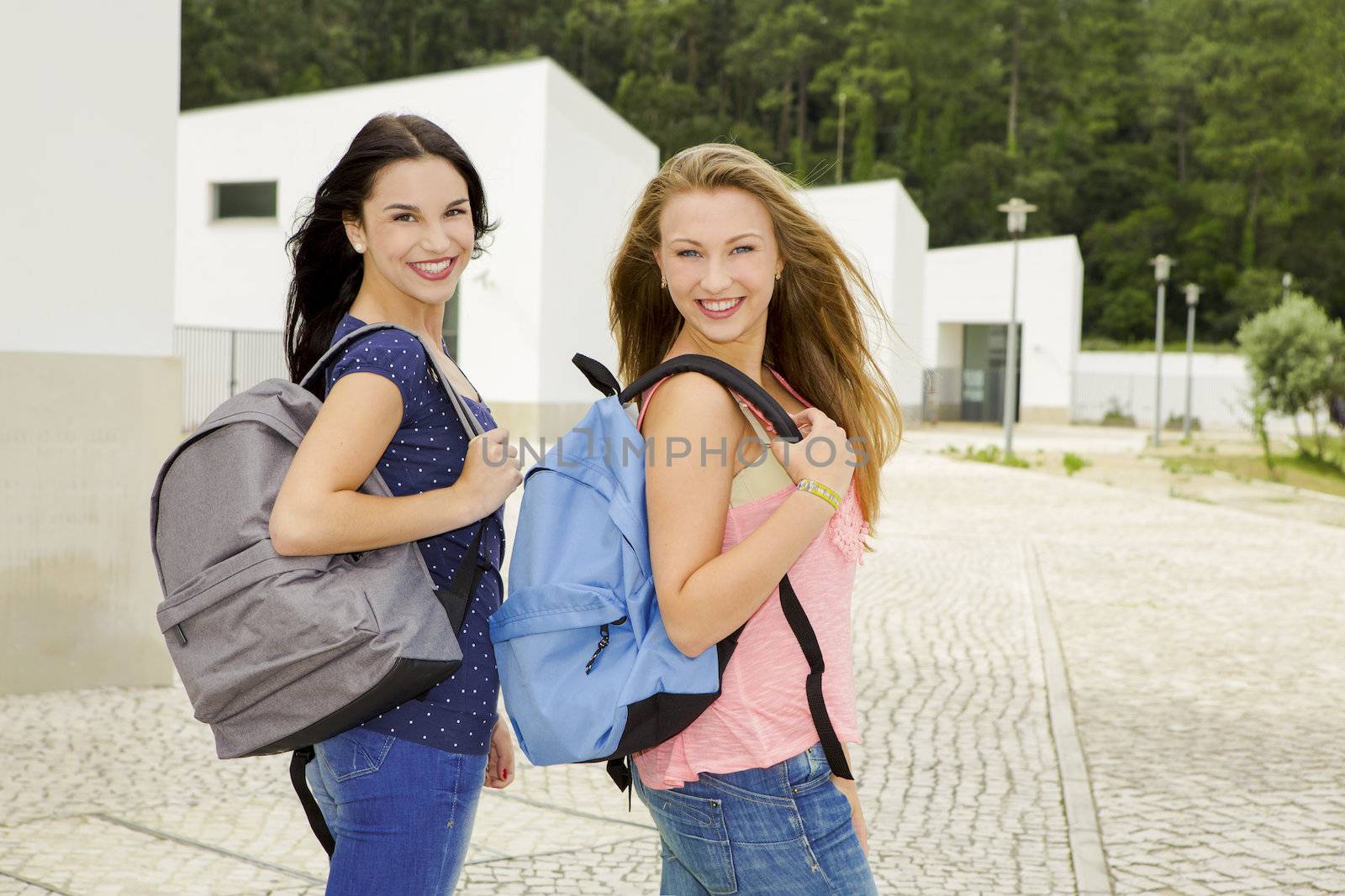 Two beautiful teenage students walking while looking back and smiling 