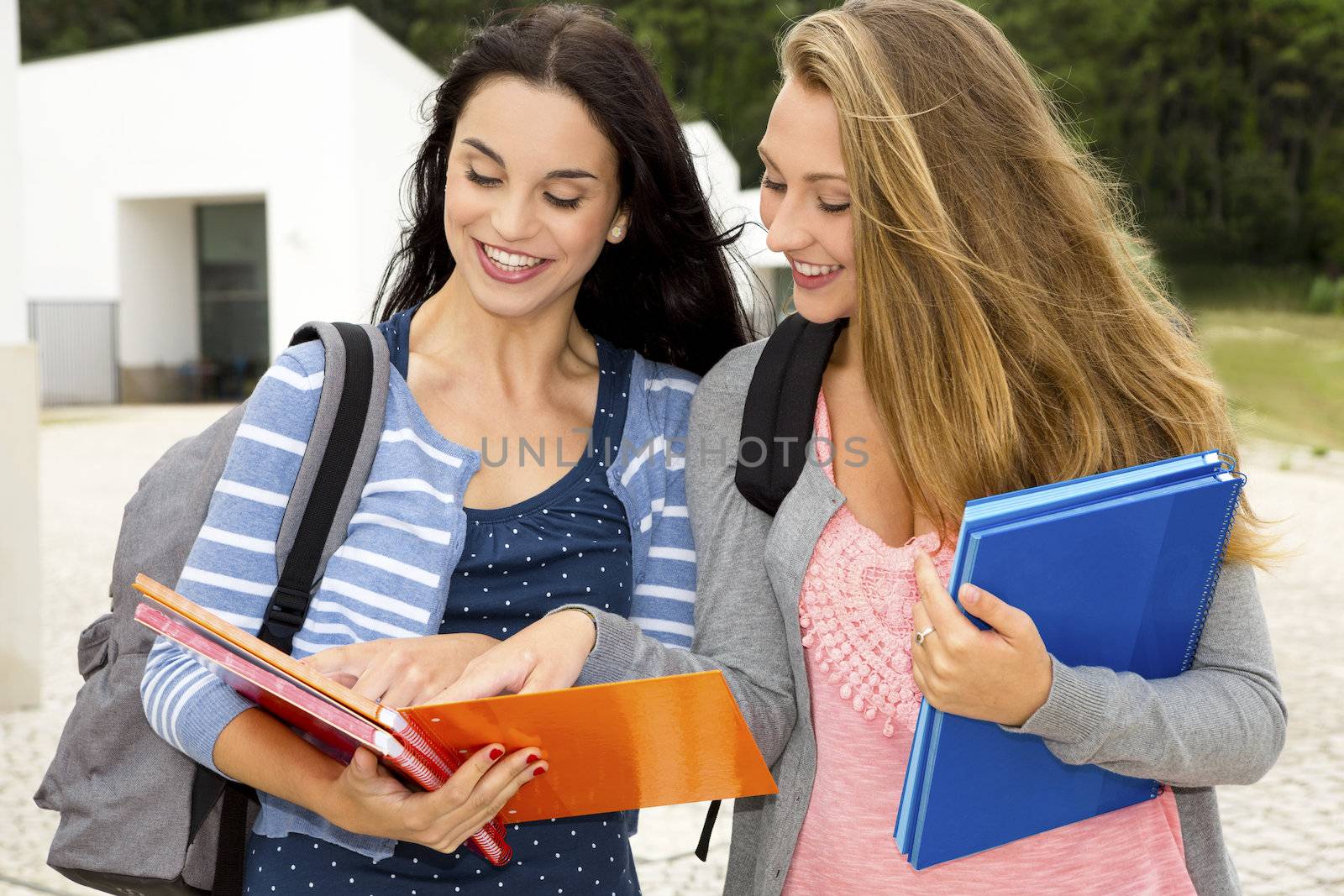 Two beautiful teenage students studying and showing something in the books