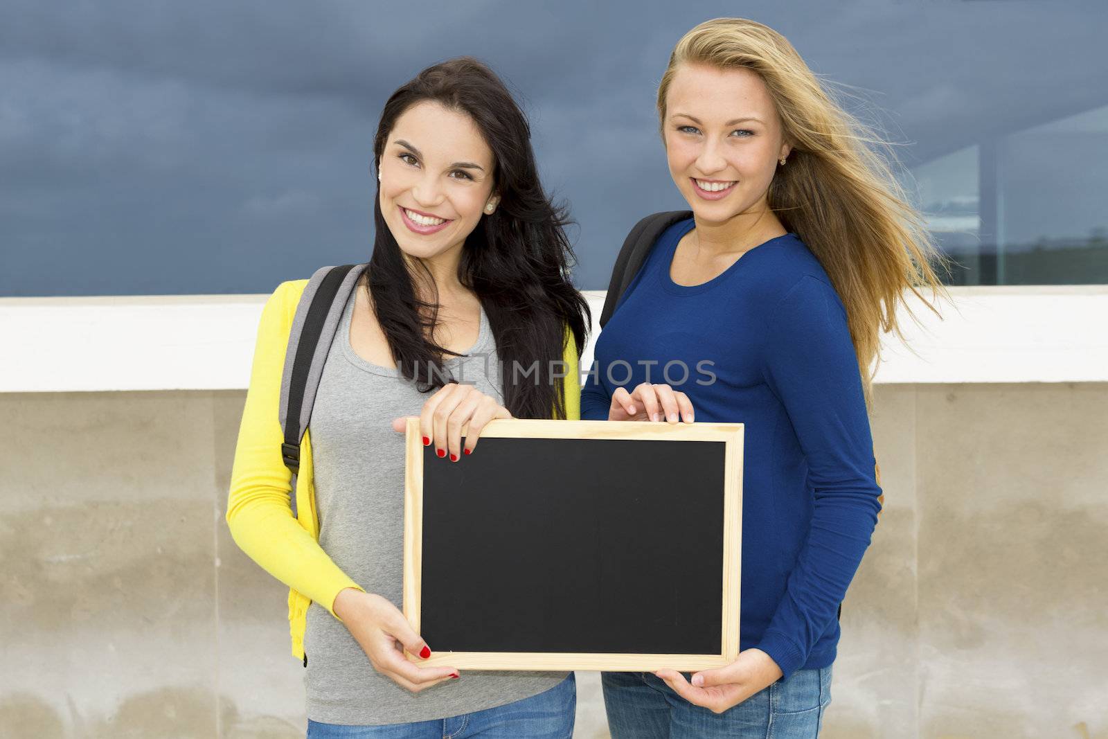 Two beautiful teenage students holding a chalkboard with the slogan Back to School