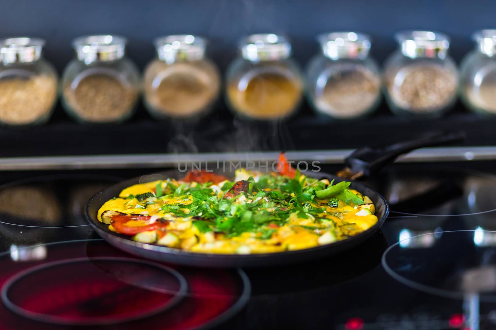 Omelet with vegetables on elecric stove and bowls with spices in the background of the kitchen.