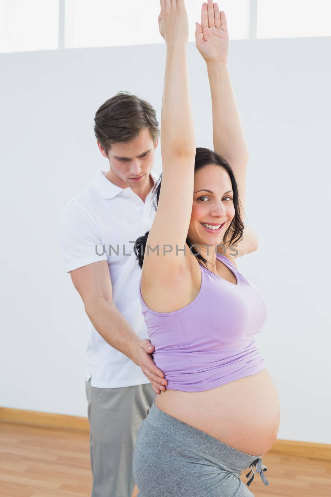 Happy pregnant woman doing yoga with a personal trainer in a fitness studio