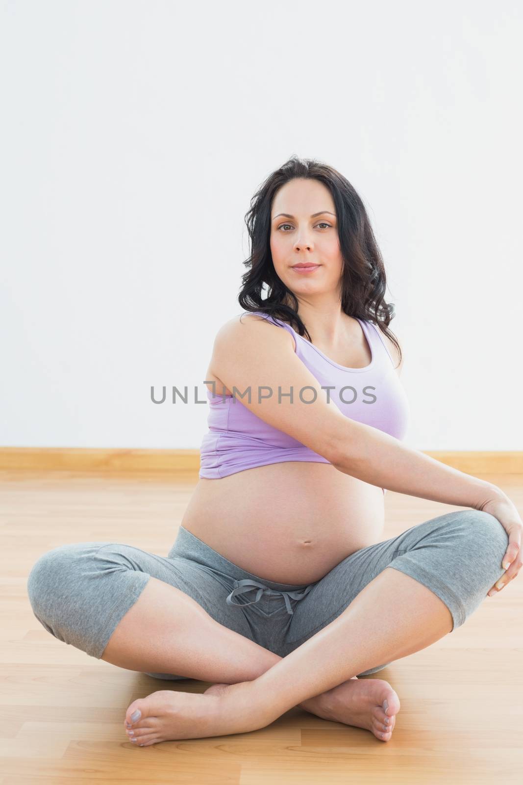 Pregnant brunette sitting on floor in lotus pose stretching in a fitness studio