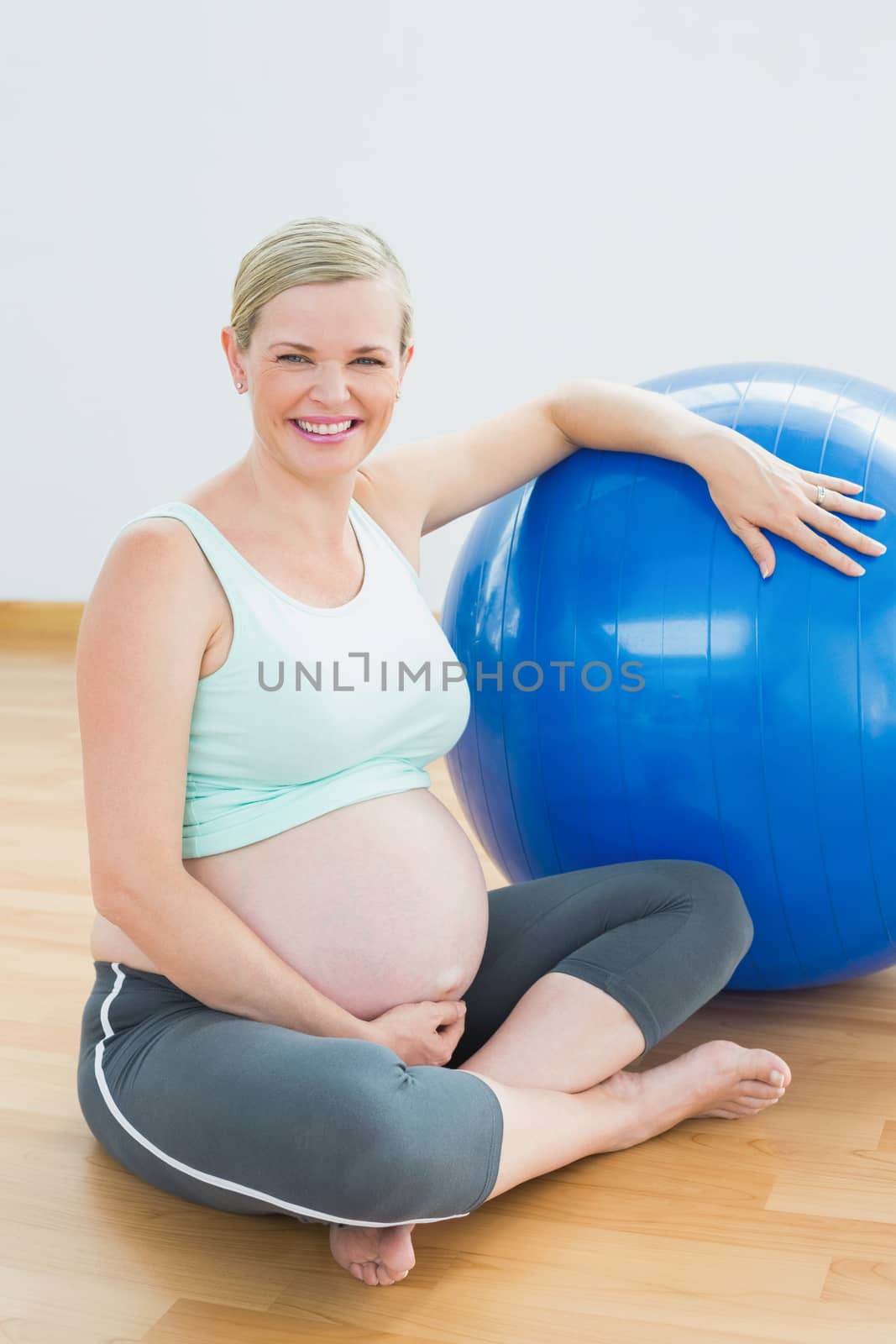 Pregnant woman sitting beside exercise ball smiling at camera in a fitness studio