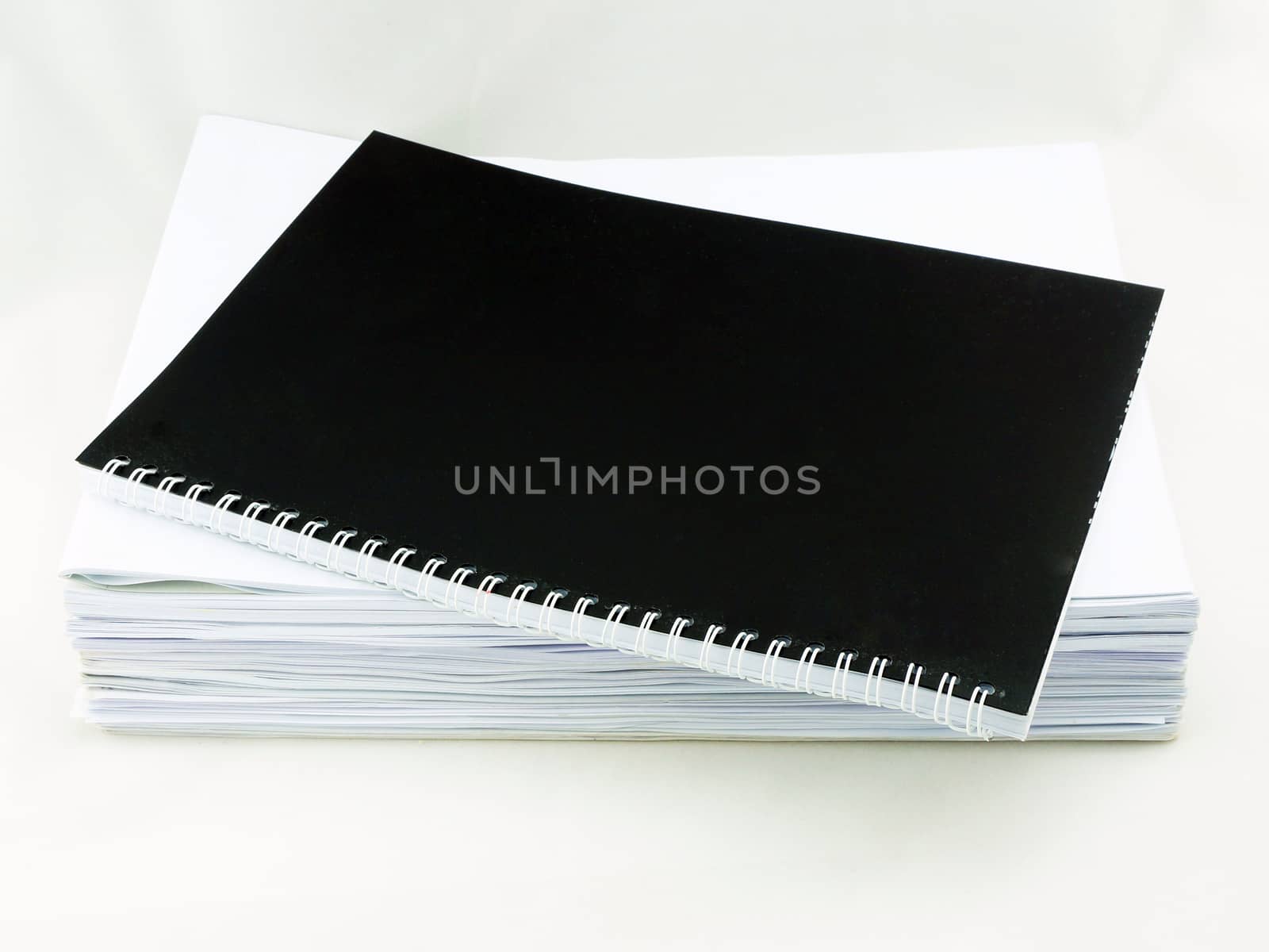 Pile of white papers arranged orderly. Black book is overlaid on top.                               