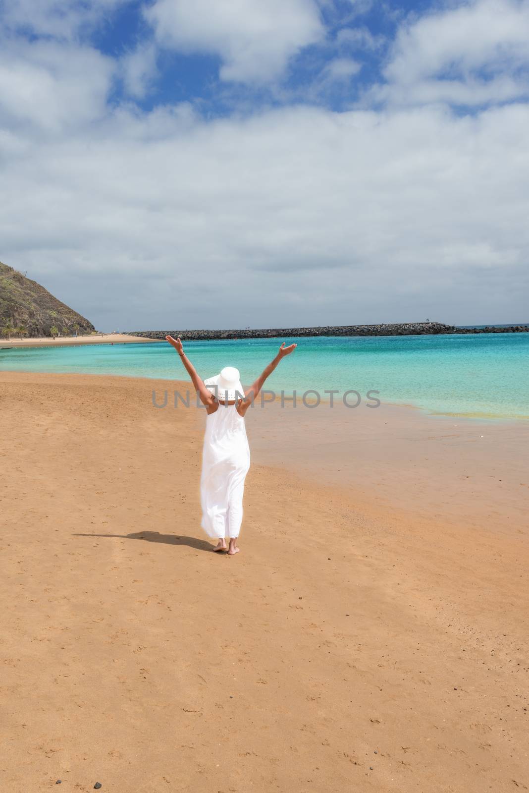 Barefoot girl in white hat and dress standing on a beach by Nanisimova