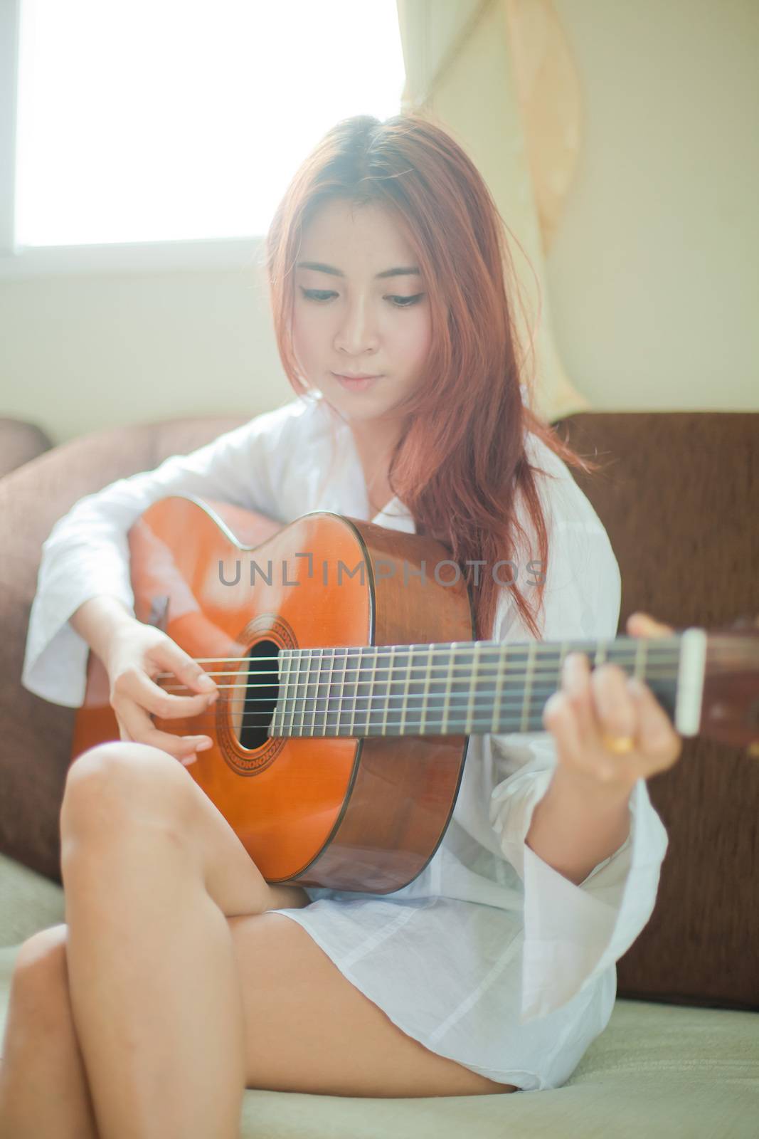 Young beautiful asian woman playing guitar in living room