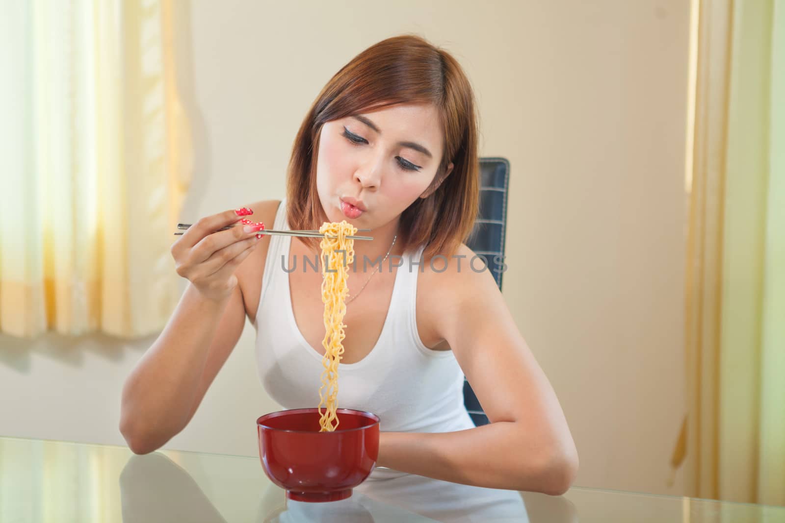 Young Asian girl eating ramen noodles using chopsticks