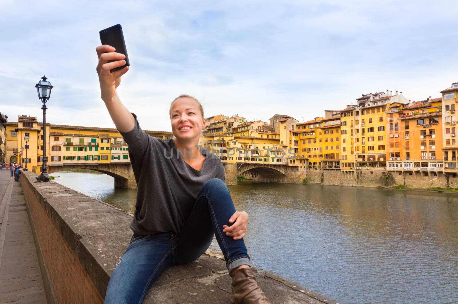 Young lady taking selfie in front of Ponte Vecchio bridge in Florence Tuscany Italy, during her summer vacations in Europe.
