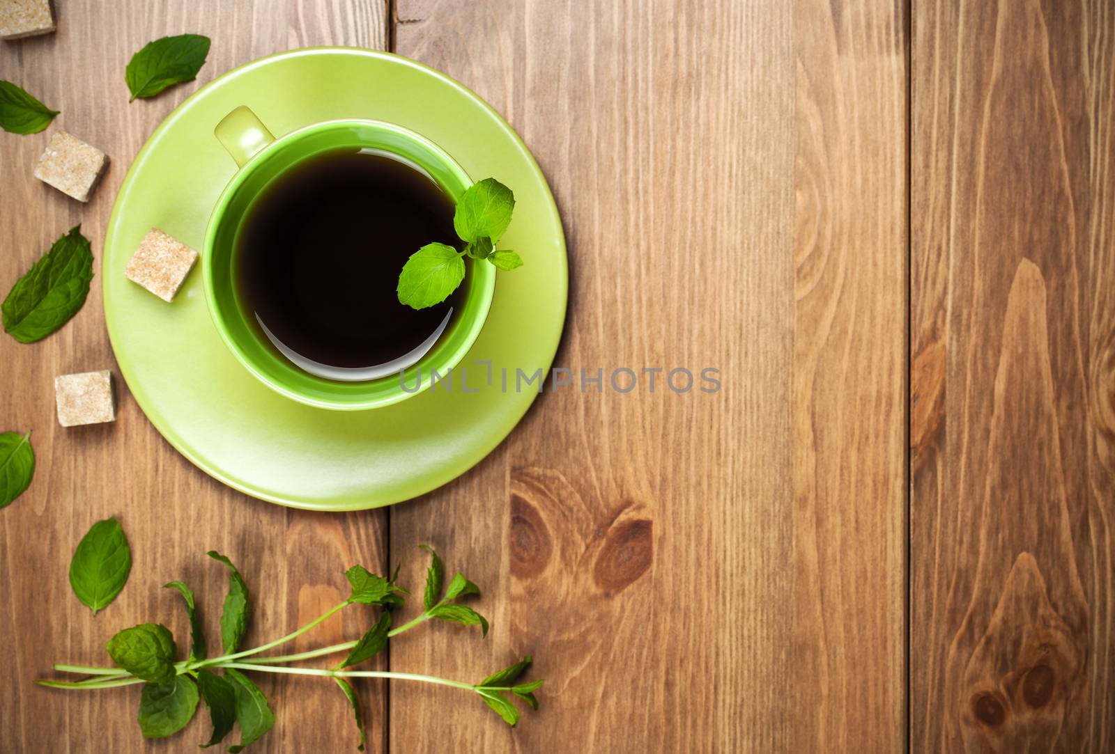 Tea mint in green cup with mint leaves and brown sugar on wooden background. Top view. Copy space. Focus on tea
