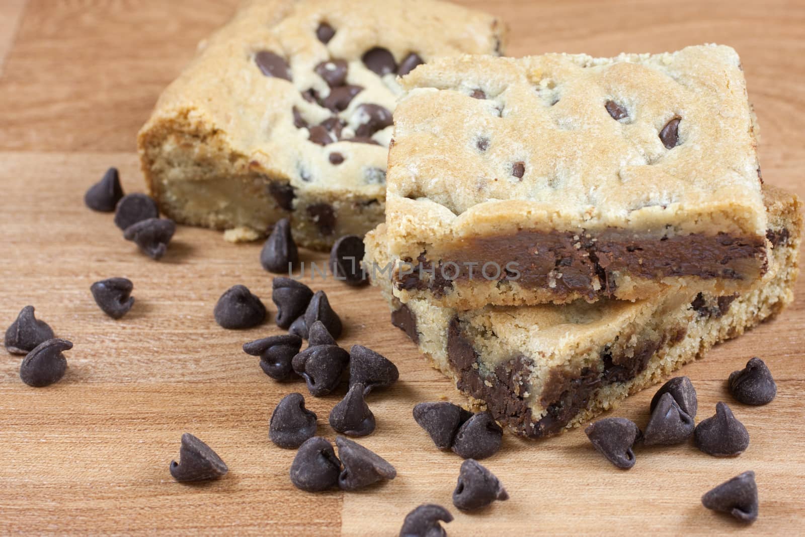 Chocolate chip cookie bars on a wooden surface with chocolate chips in the forground.