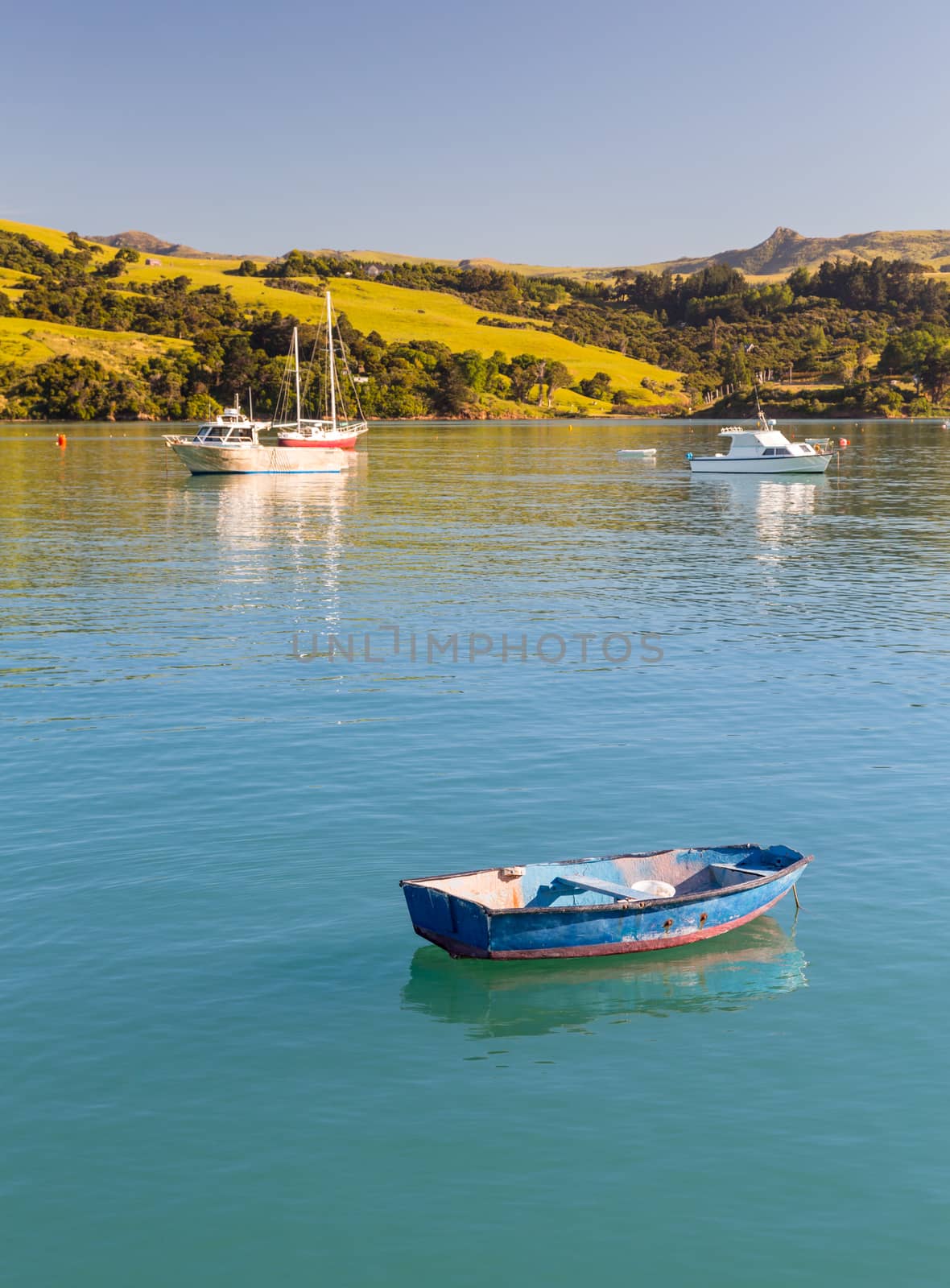 Old weathered blue rowing boat moored in Akaroa Harbor in New Zealand with other yachts in the background