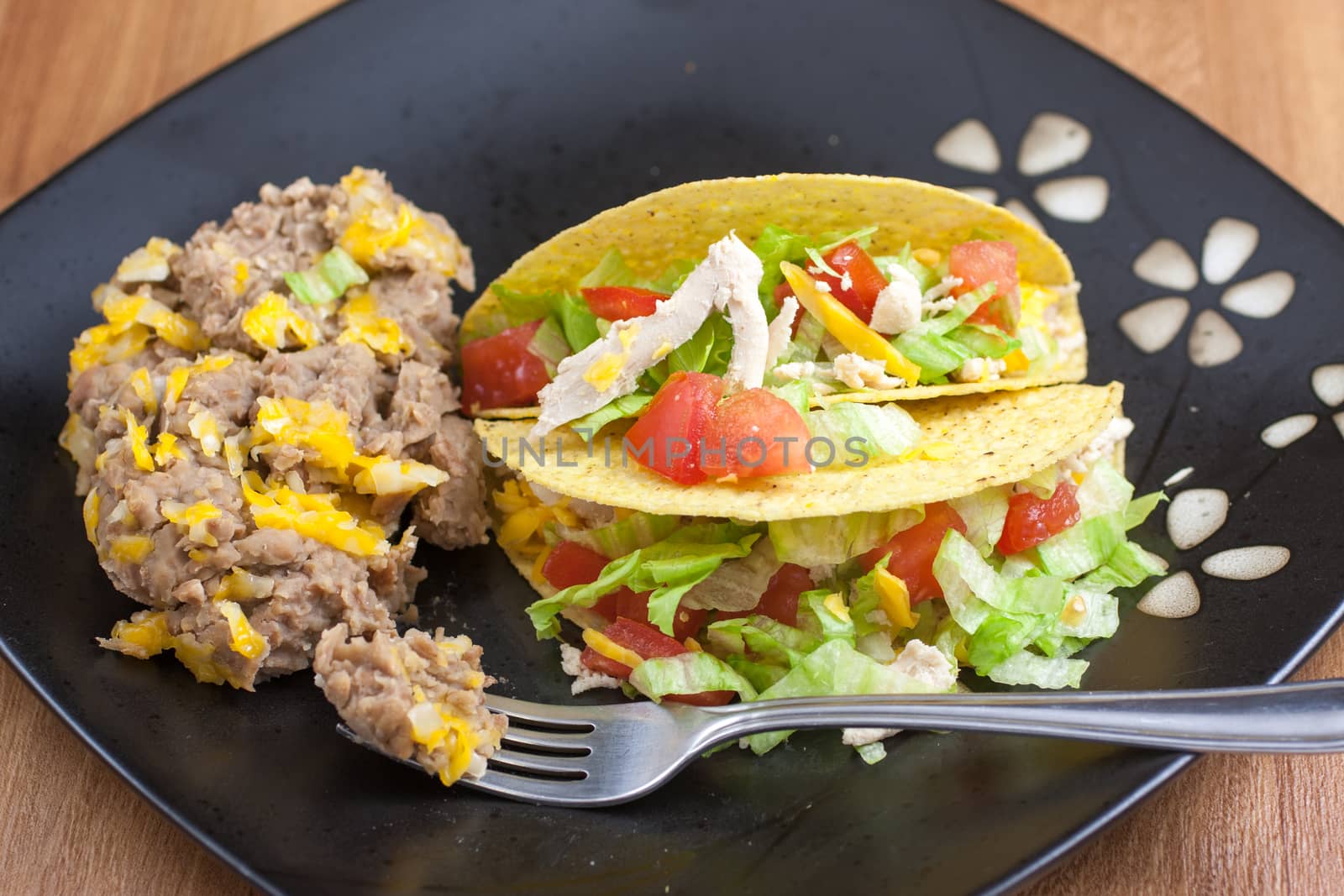 Tacos and refried beans on a dark plate, sitting on a wooden table.