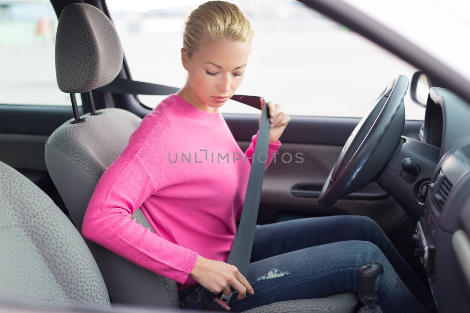 Safety first. Beautiful blonde caucasian lady fastening car seat belt.