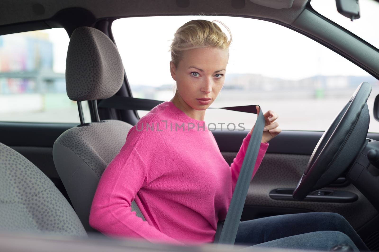 Safety first. Beautiful blonde caucasian lady fastening car seat belt.