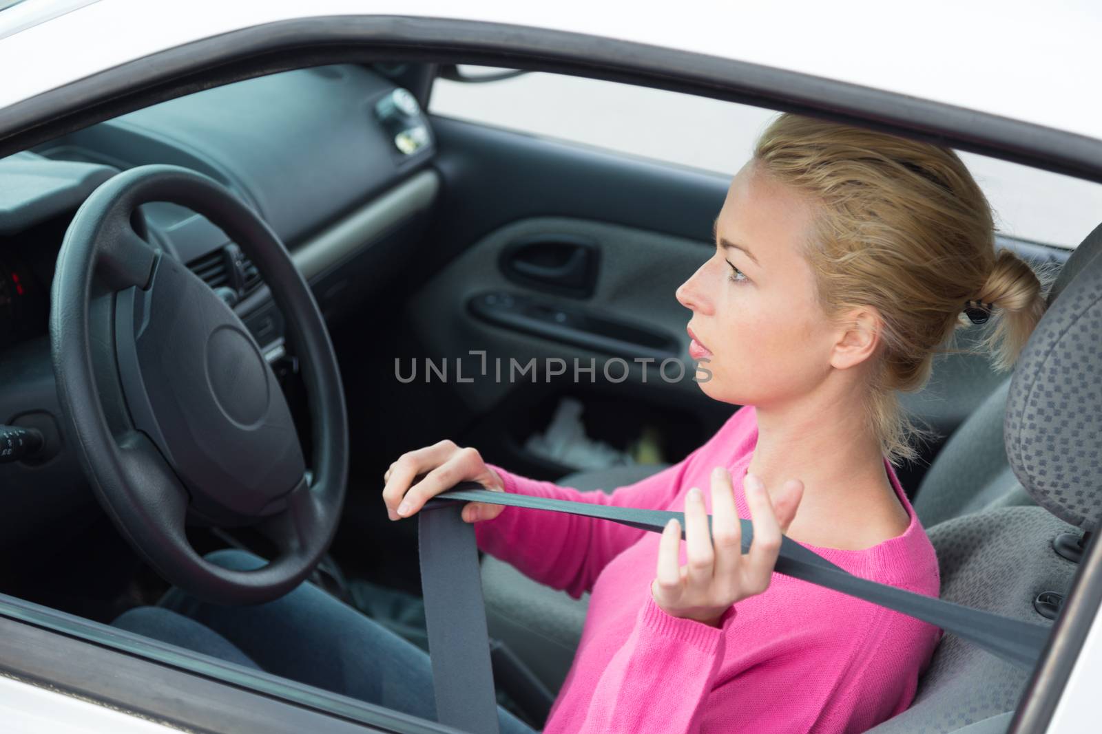 Safety first. Beautiful blonde caucasian lady fastening car seat belt.