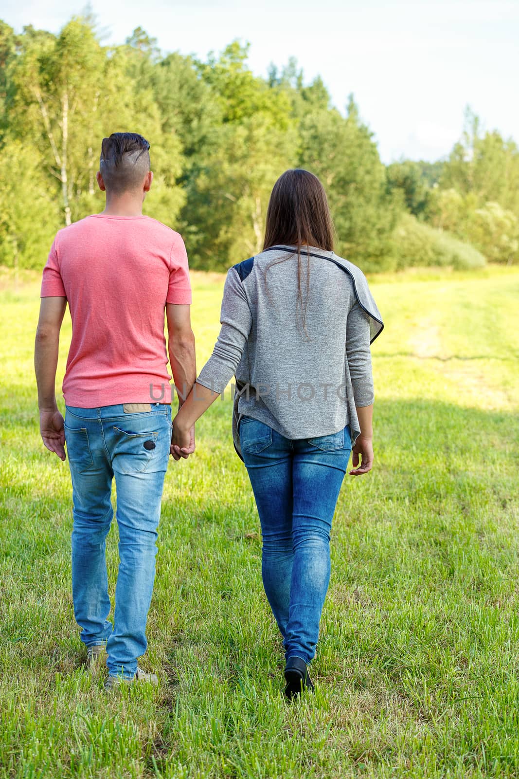 Rear view of young couple walking outdoor in sunny summer day