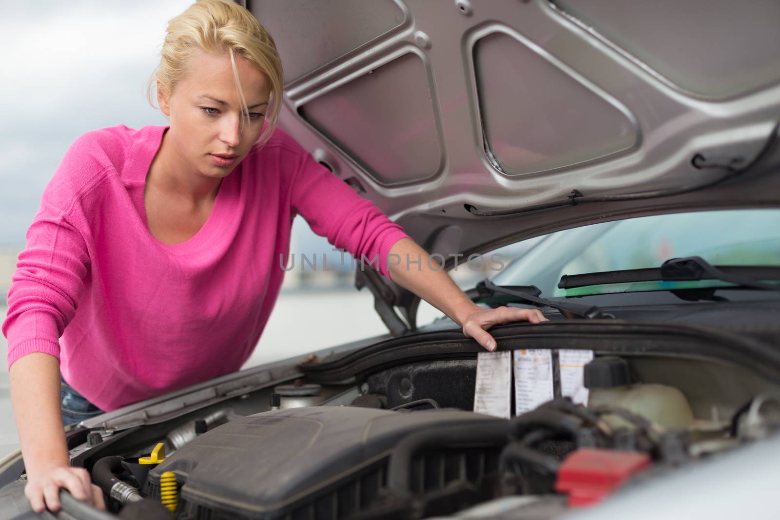Self-sufficient confident modern young woman inspecting broken car engine.