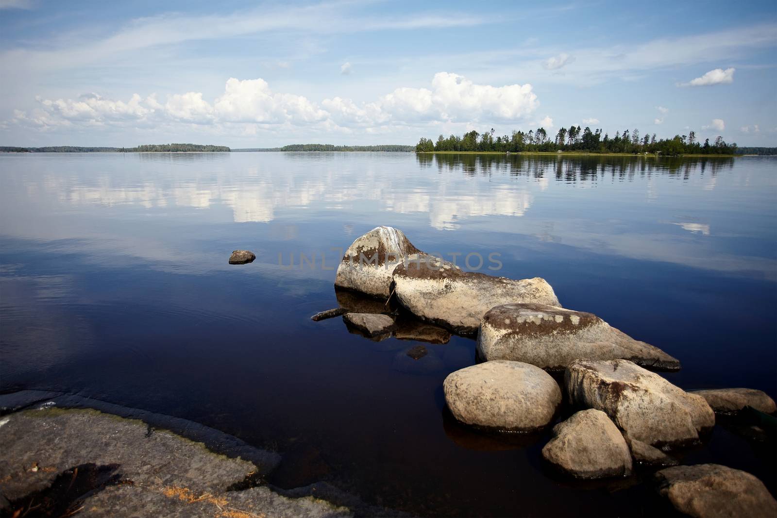 Water landscape with stones. Stones in water. The lake with stones. Beautiful landscape. Water smooth surface and the blue sky with clouds.