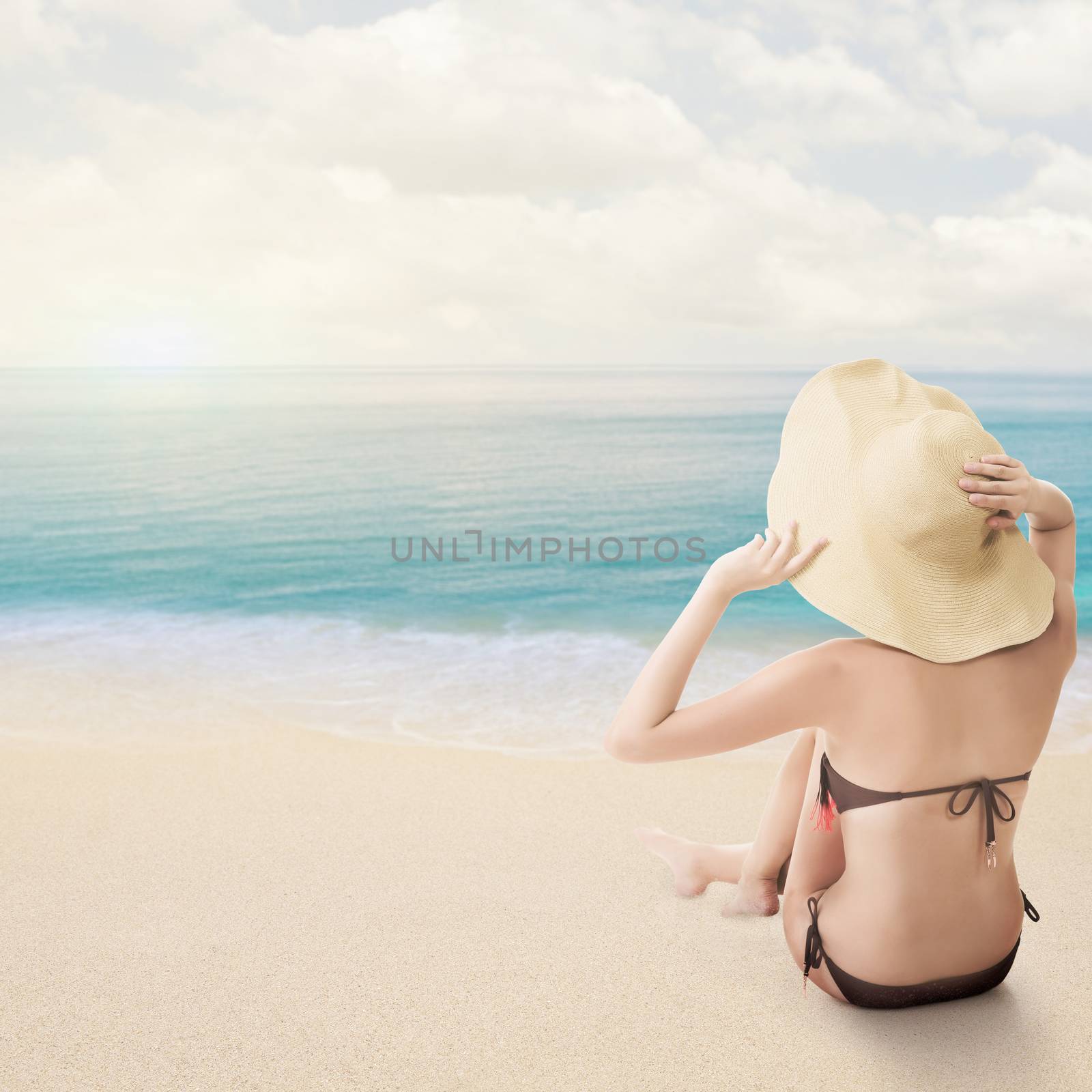 Attractive bikini beauty of Asian sit on beach and looking far away, rear view with copyspace.