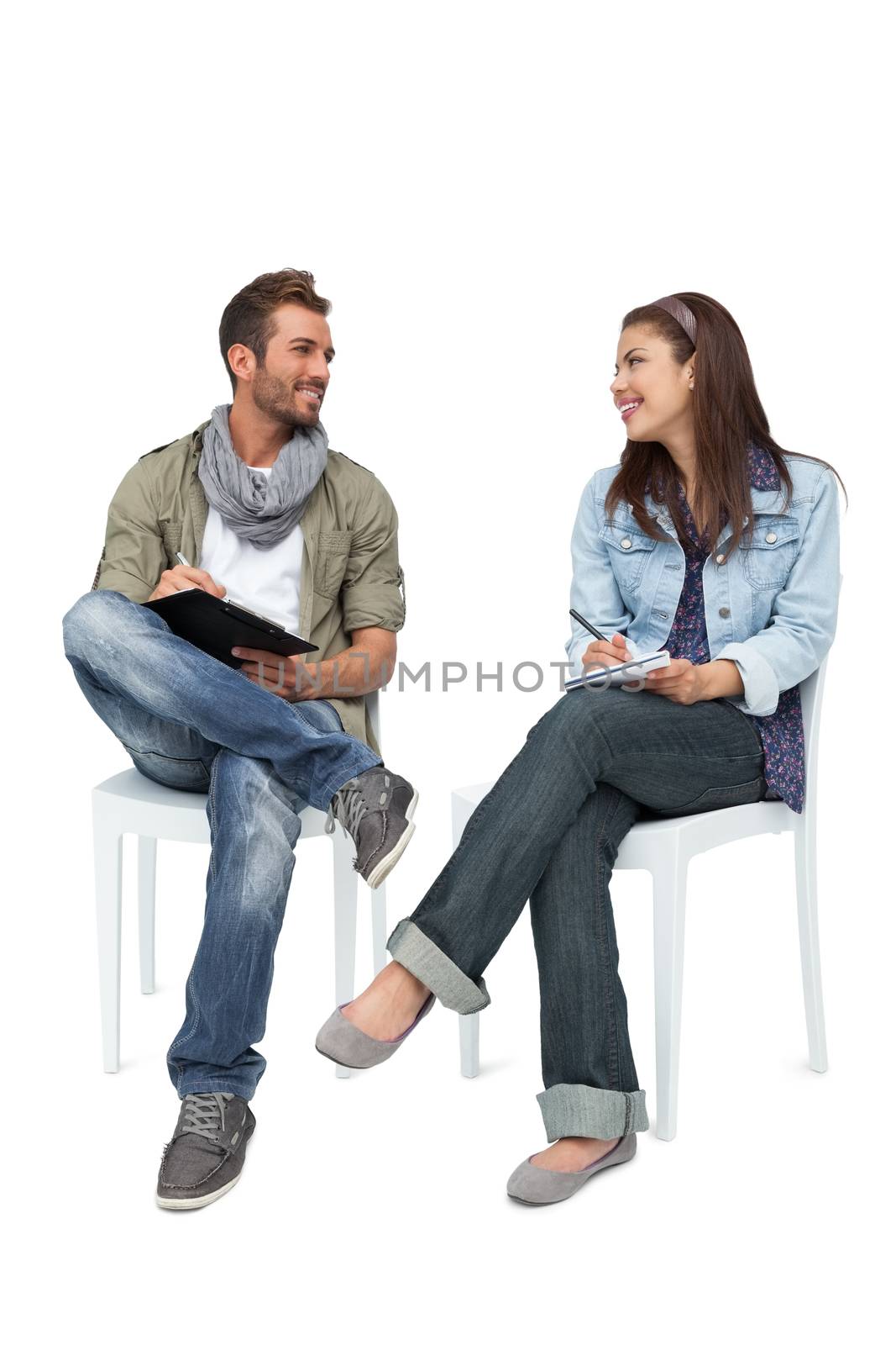 Full length of a cool young couple writing in notepads over white background