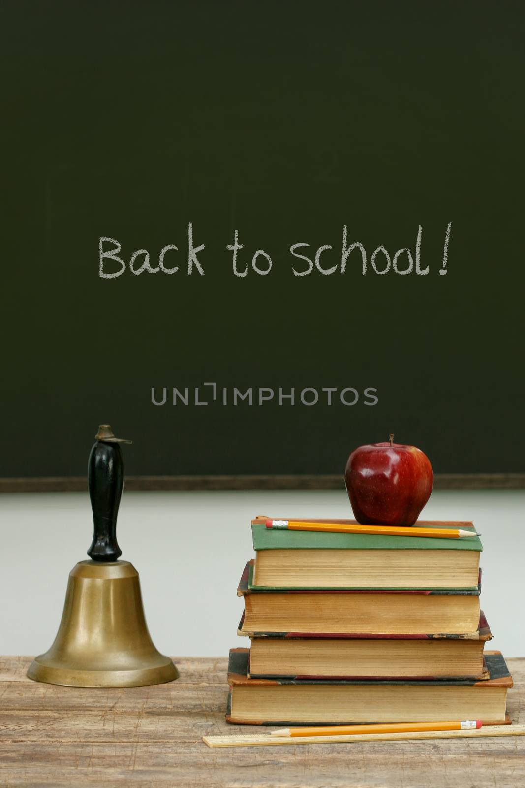 School bell and books on desk with chalkboard by Sandralise
