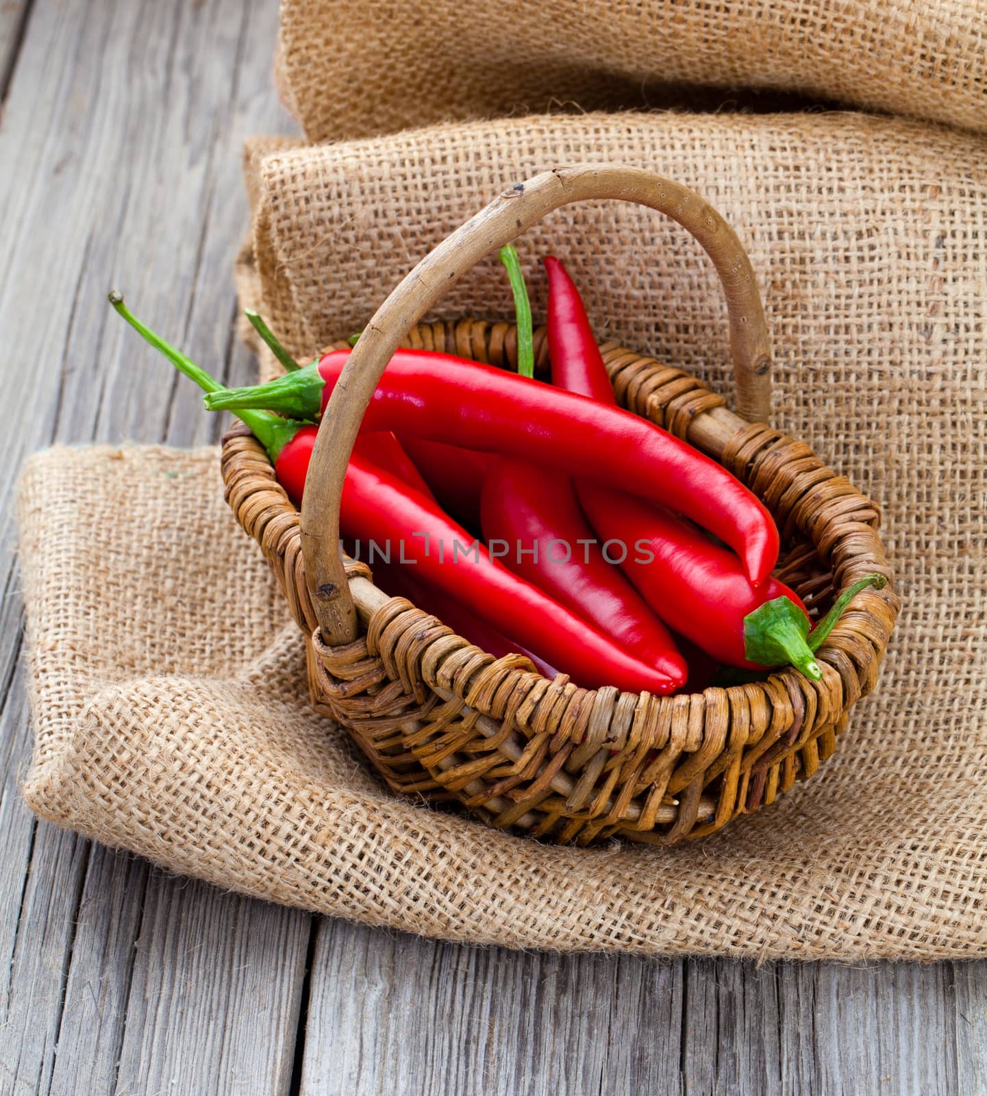 Red chili pepper in a wicker basket with burlap on the wooden ba by motorolka